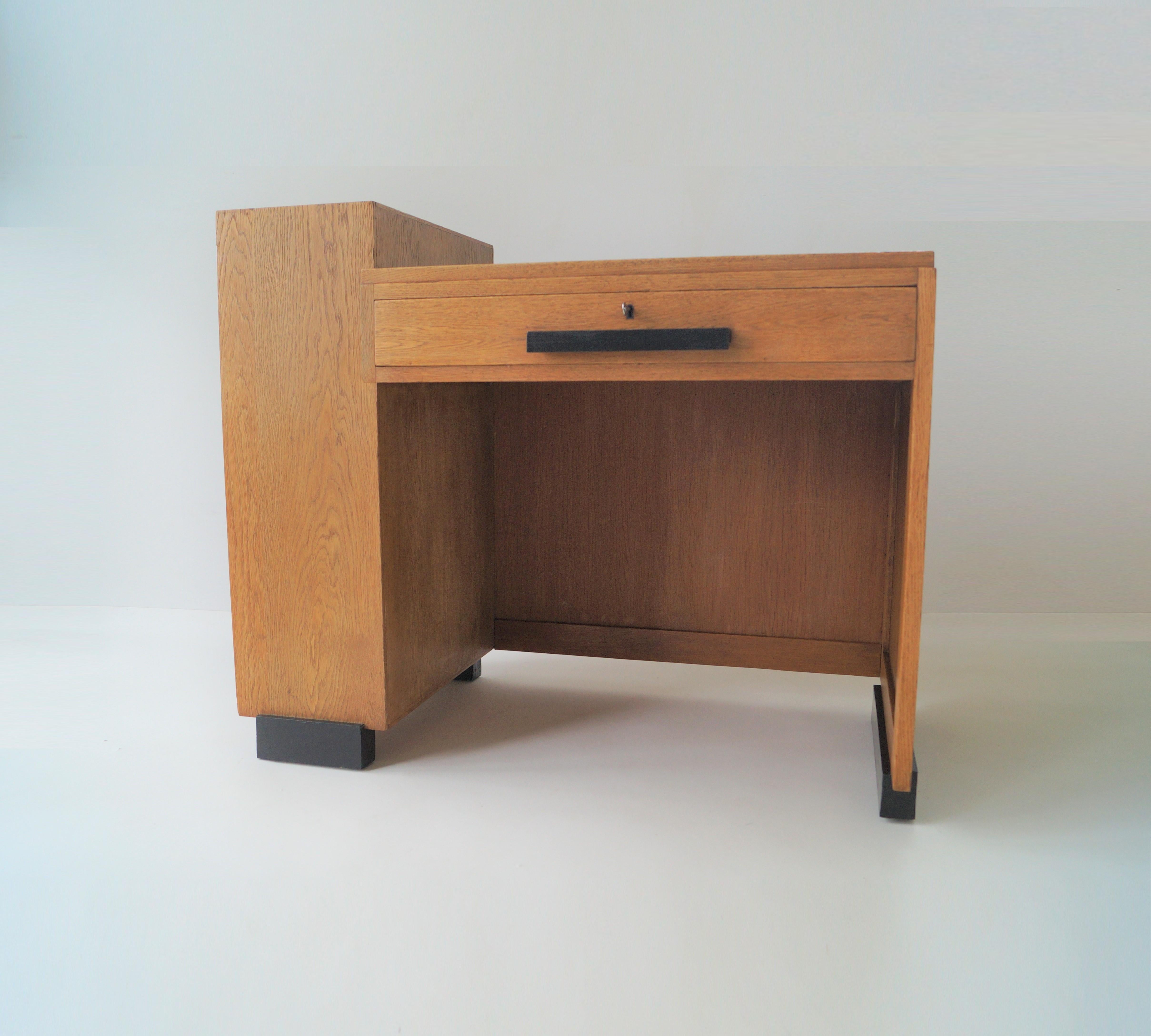 A modestly sized modernist writing desk with an assymetrical design, giving it a Haagse School/modernist appearance.

It has one large drawer at the front and a three shelve storage compartiment at the left. On the desktop a black leather inlay. The