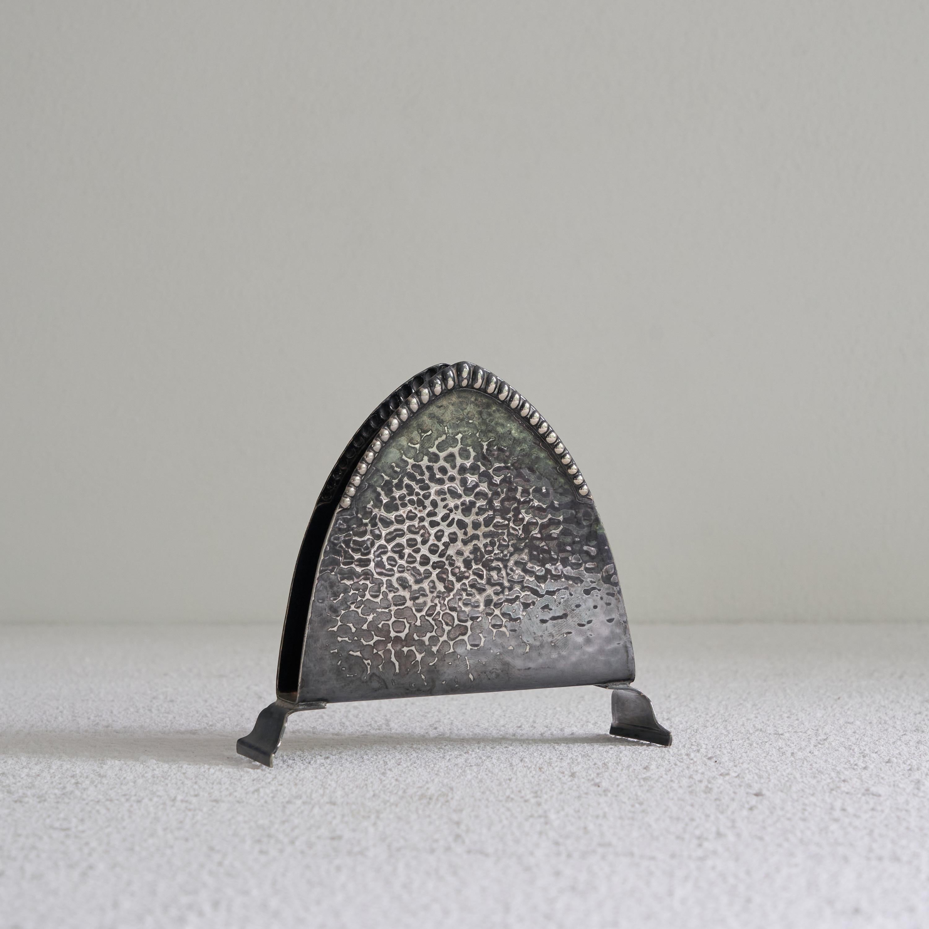 Dutch Art Deco napkin holder in patinated silver. The Netherlands, early 20th century. 

Beautiful and very elegant napkin holder in a distinct Art Deco / Amsterdamse School style. Very good design with a triangular base shape decorated with