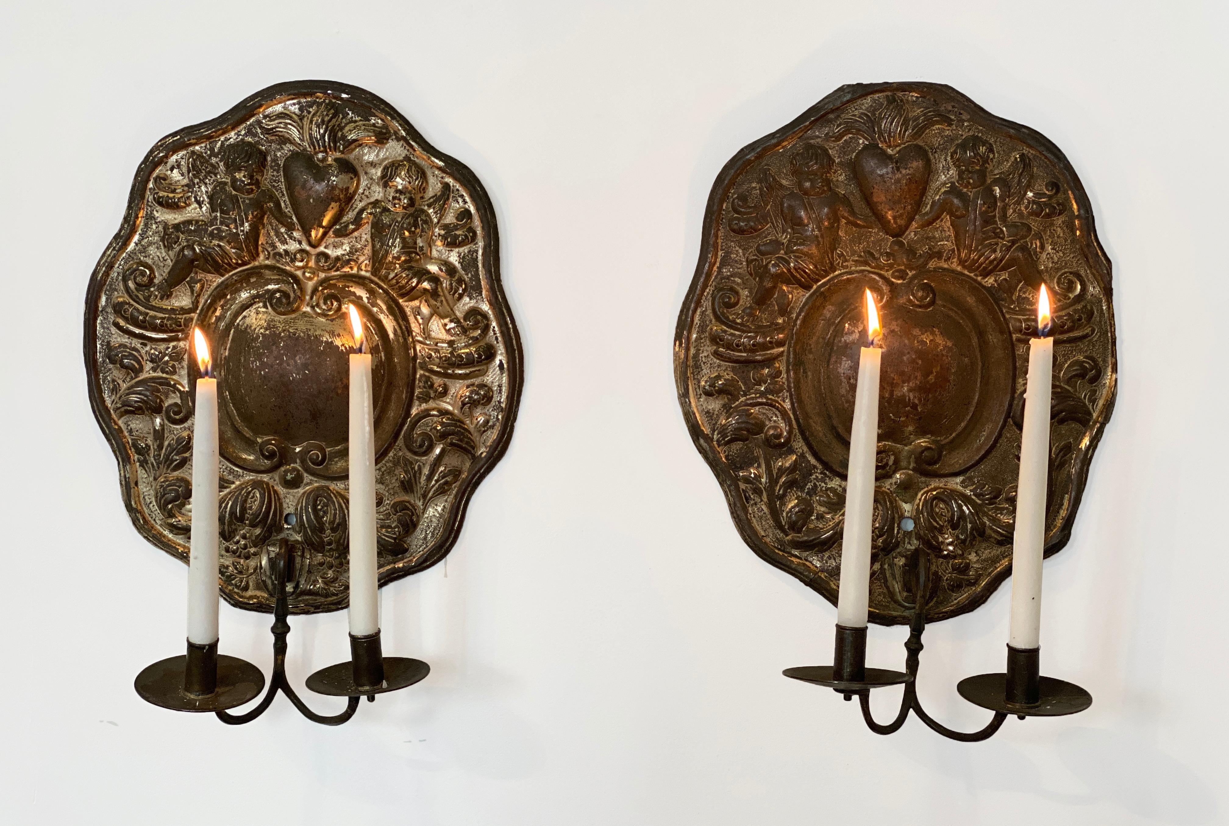 Pair of Dutch Baroque double-arm sconces, origin: Holland, circa 1760, silver plate repoussé.

Two candle arms with back plates decorated with centre cartouche surrounded by cherubs / putti, foliage and charming hearts. 

We also sell bespoke,