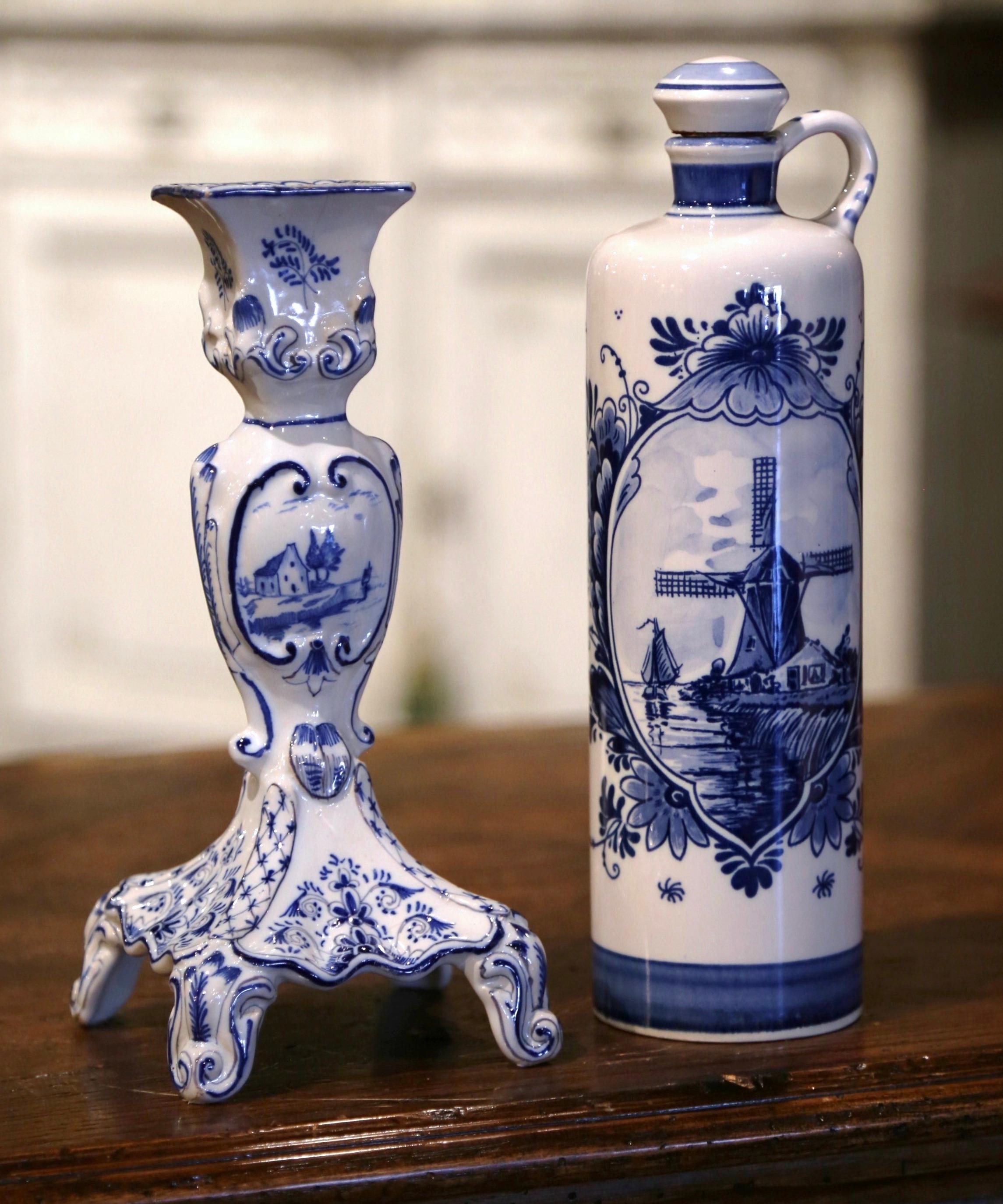 Decorate a shelf or kitchen counter with these elegant antique Delft pieces. Crafted in Holland circa 1940, the set includes a tall olive oil bottle with cork top, and a candle holder. Both items are decorated with hand painted windmill and sailboat