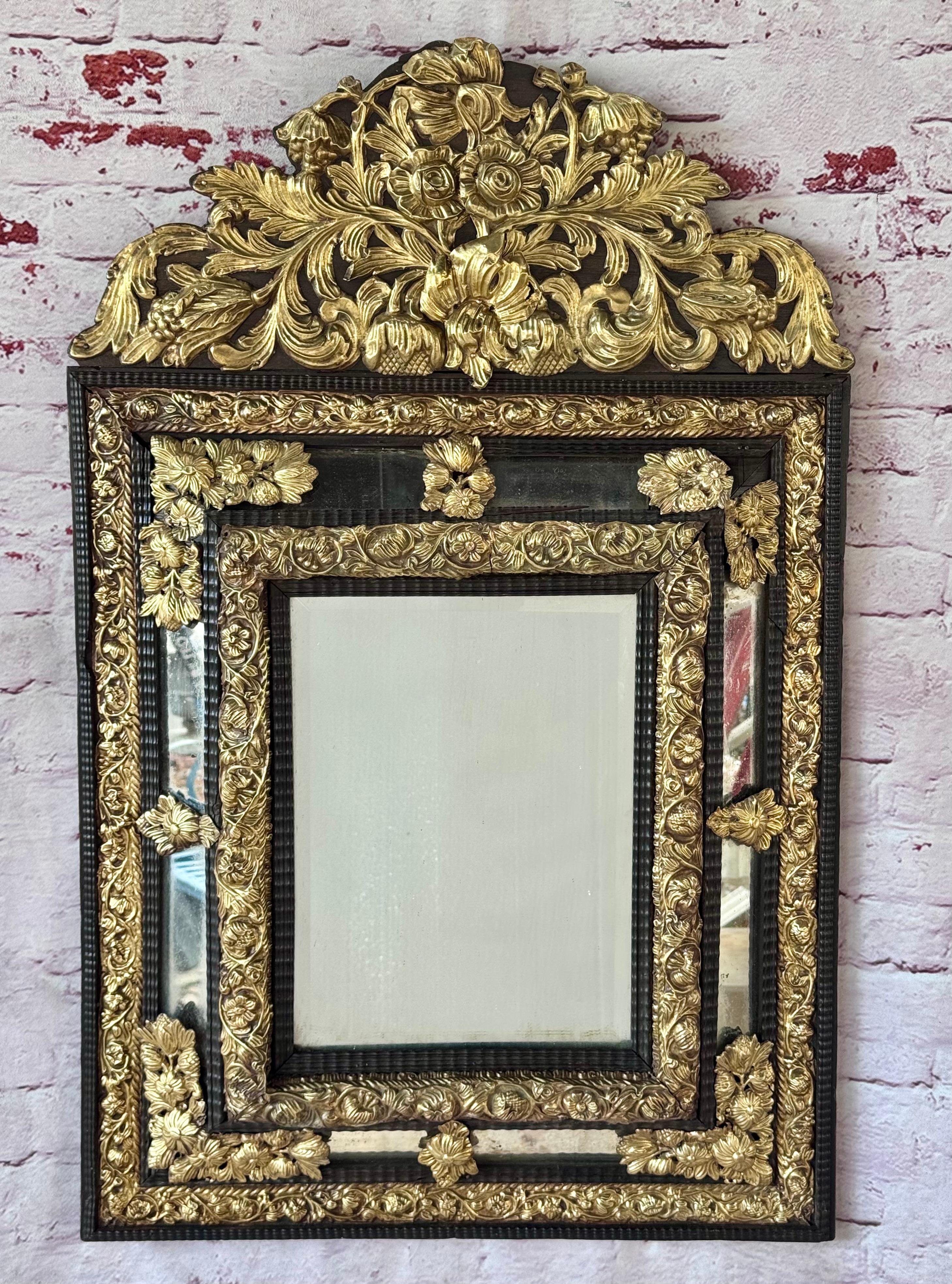 Espejo Holandés del Siglo XIX de Latón y Madera Ebonizada. El espejo tiene un marco de madera ebonizada adornado con intrincados apliques de latón dorado. El espejo presenta una elaborada cresta de hojas de acanto y flores, símbolo de la opulencia y