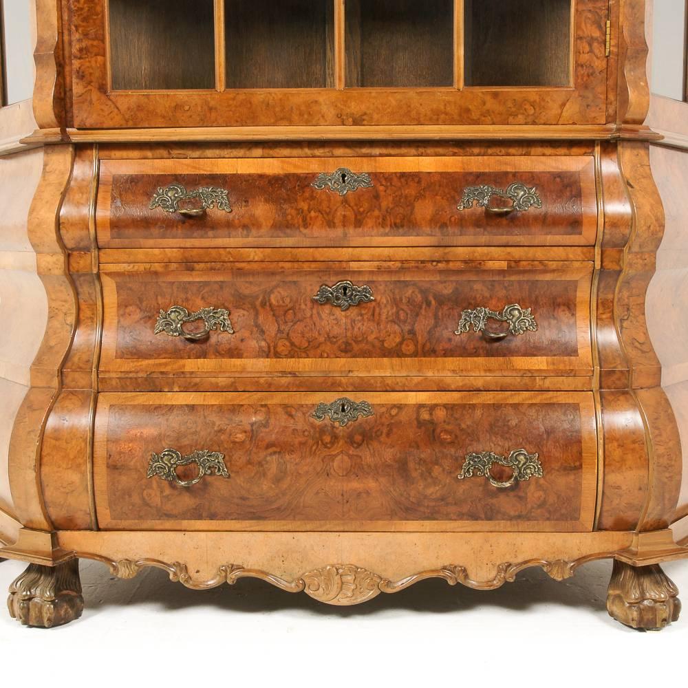A fine Dutch China cabinet, or vitrine, in burl walnut, the top with a single glass door, the three-drawer base of dramatic ‘bombe’ form, circa 1940.



 