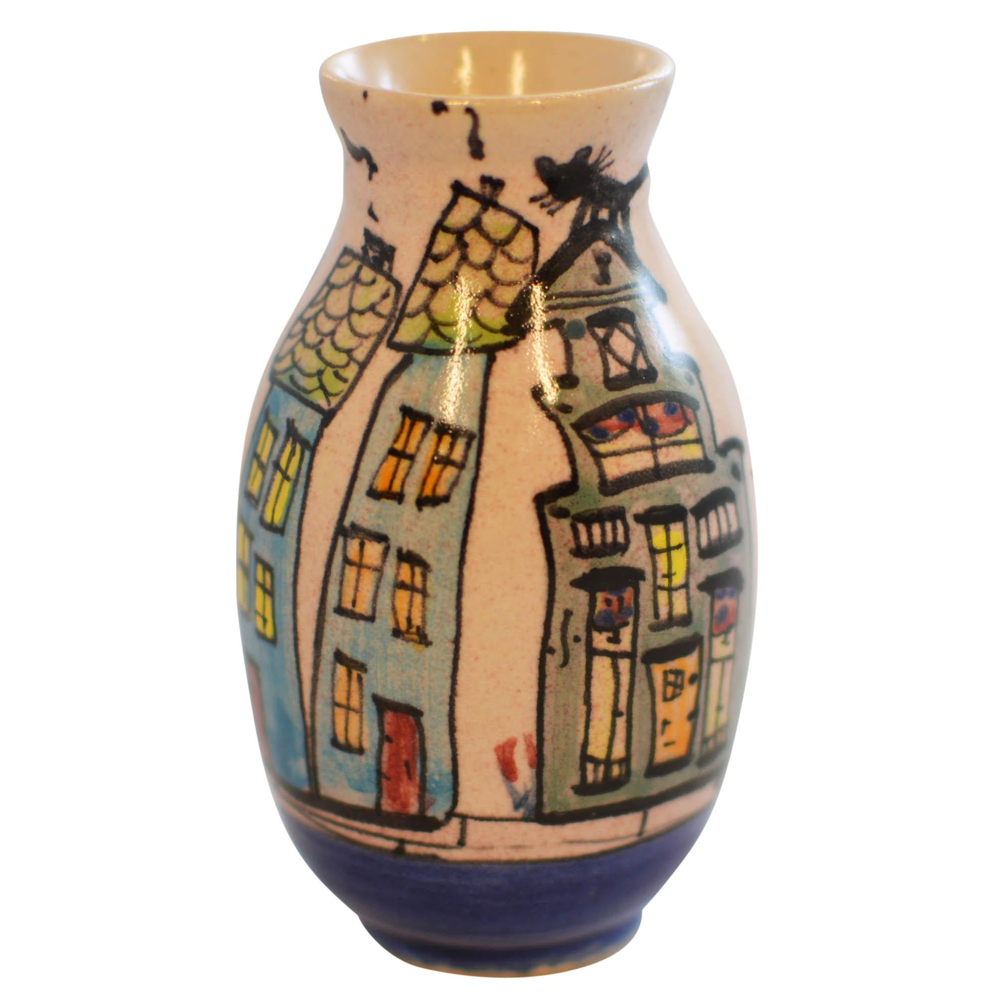 handcrafted bud vase is the work of Anna Maria Preuss. The vase features a scene of hand painted canal front homes with whimsical cat atop a gray house. Anna's mark is on the bottom. Vase measures 2.75
