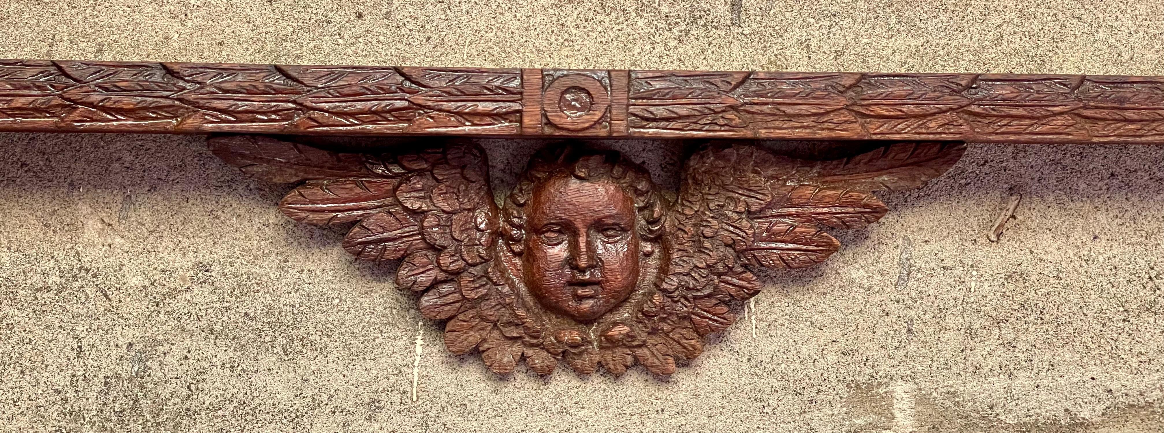 This is the sweetest carved oak plate display rack with a beautiful cherub face surrounded by intricate wings in the center bottom and circles on either end and center of the slats with stylized leaves radiating from the center and stylized circles