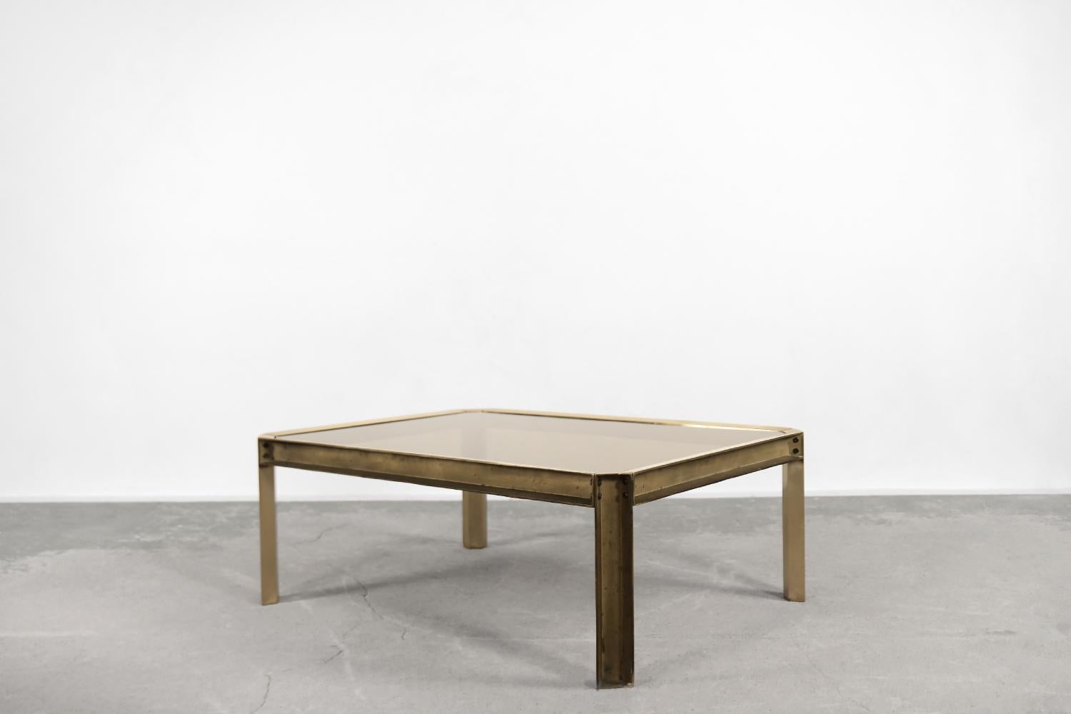 This large T09 Embassy coffee table was designed by Peter Ghyczy in 1972. I was handcrafted from cast brass and a smoked glass top. The inner surface was finished in raw way, in a brutalist style. The roughness and naturalness of the metal are
