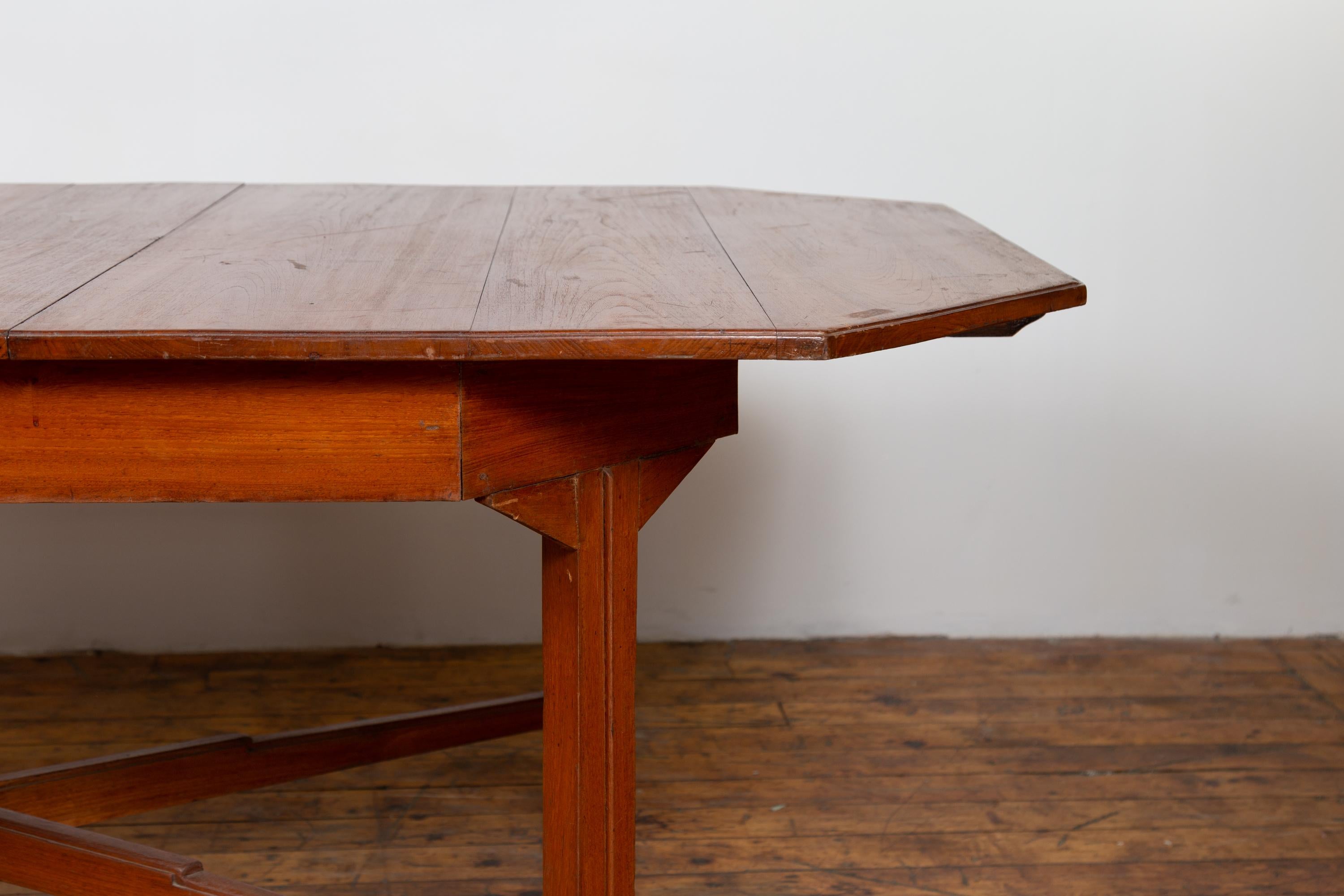 An antique Dutch Colonial period Javanese extension dining table from the early 20th century, with canted corners and folding leaf. Born on the island of Java during the early years of the 20th century, this handsome dining table features a