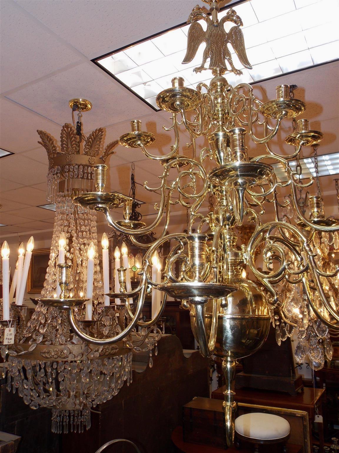 Dutch Colonial brass three-tiered eighteen light chandelier with double headed eagle medallion, scrolled decorative arms, original bobeches, centered bulbous column and terminating on a large lower ringed ball with ring finial. Chandelier is candle
