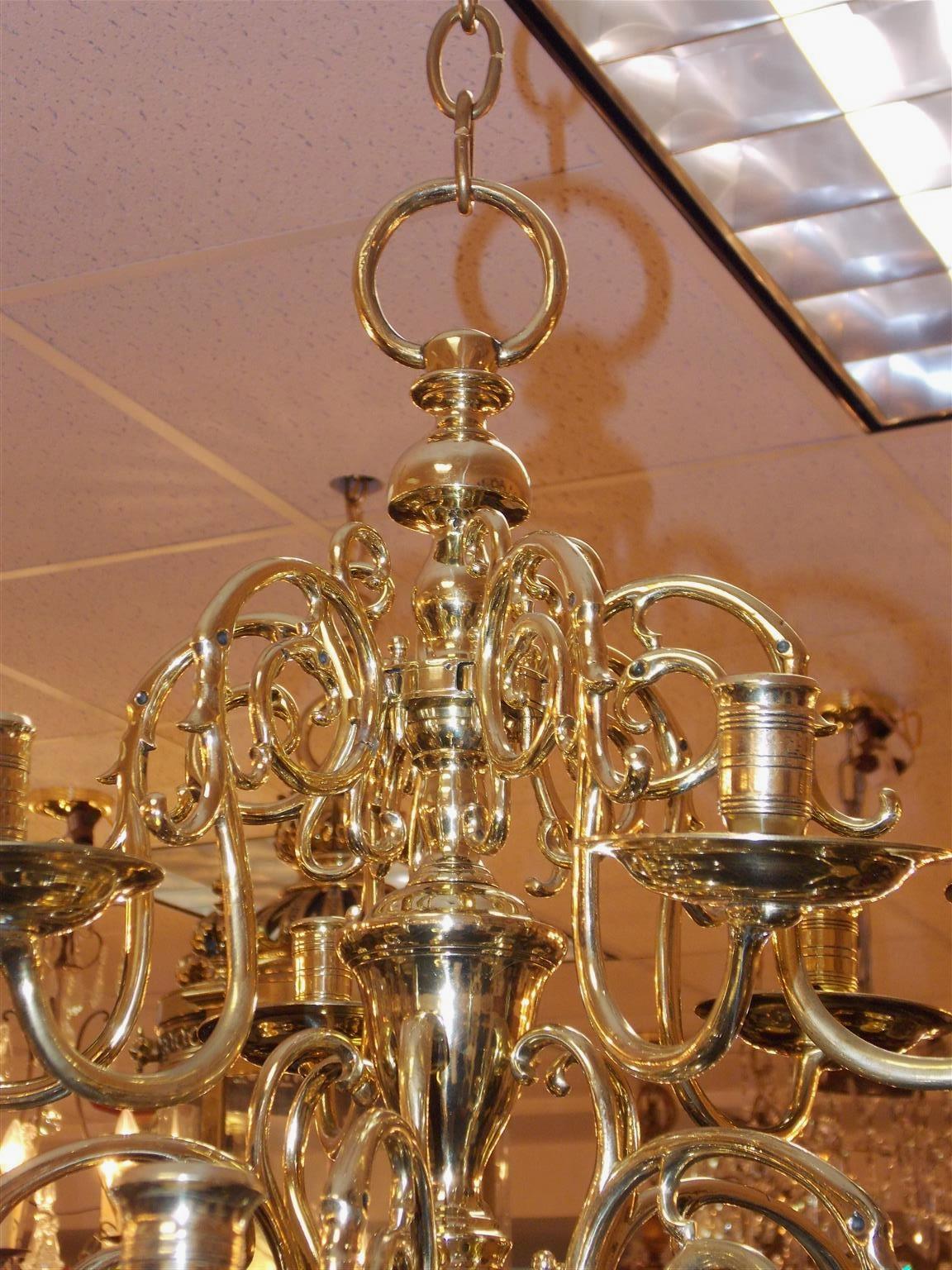 Dutch colonial brass two-tiered twelve light chandelier with scrolled decorative arms, original bobeches, centered bulbous urn column, and terminating on a lower large ball with ring finial. Candle powered and can be electrified if desired, Mid-18th