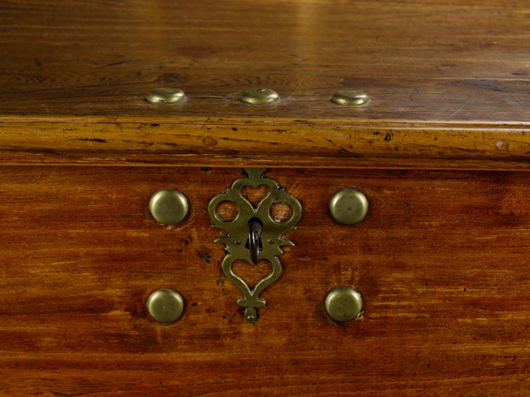 Questa cassapanca antica del XVIII secolo, probabilmente proveniente dal Nord Europa o da una colonia olandese, è realizzata in legno di olmo. Presenta raccordi in ottone a forma di cuore, cerniere in ferro, maniglie in metallo nero e solide gambe