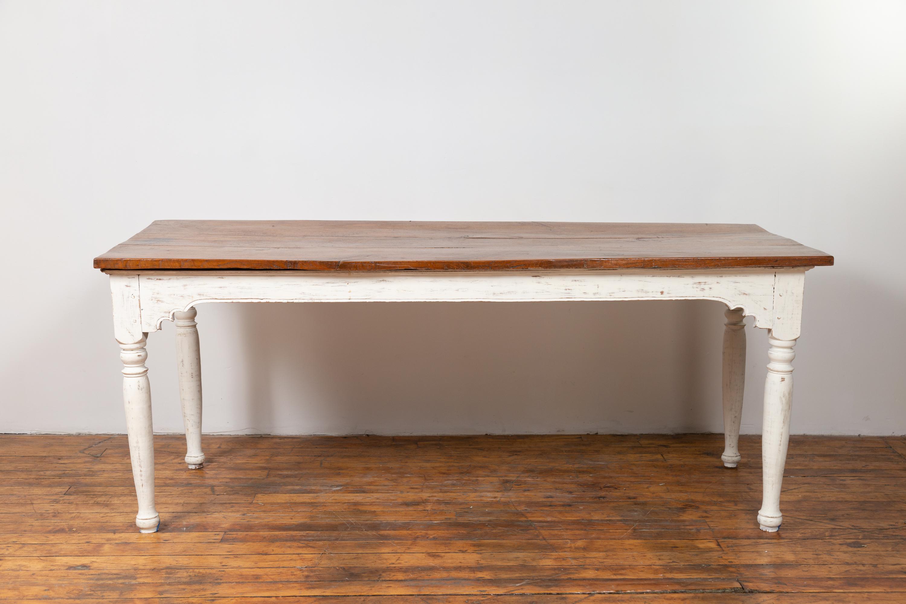 A Dutch Colonial Indonesian teak wood dining table from the early 20th century, with white painted base and turned legs. Found in Jakarta, this charming teak wood dining table features a rectangular three-plank top sitting above a lovely white