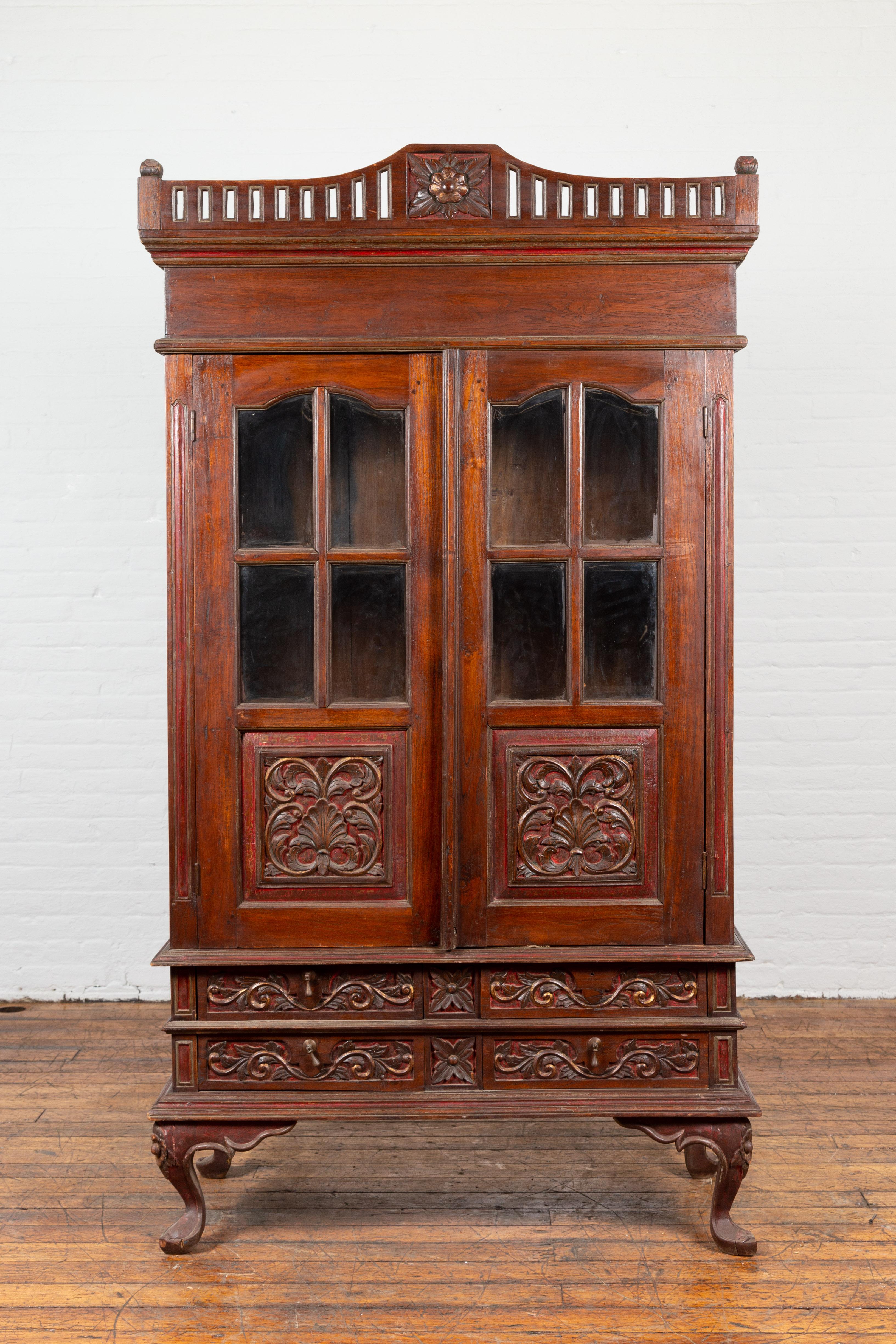A Dutch Colonial period Indonesian display cabinet from the early 20th century, with carved motifs, glass doors and cabriole legs. Created in Indonesia during the early years of the 20th century, this Dutch Colonial display cabinet features an