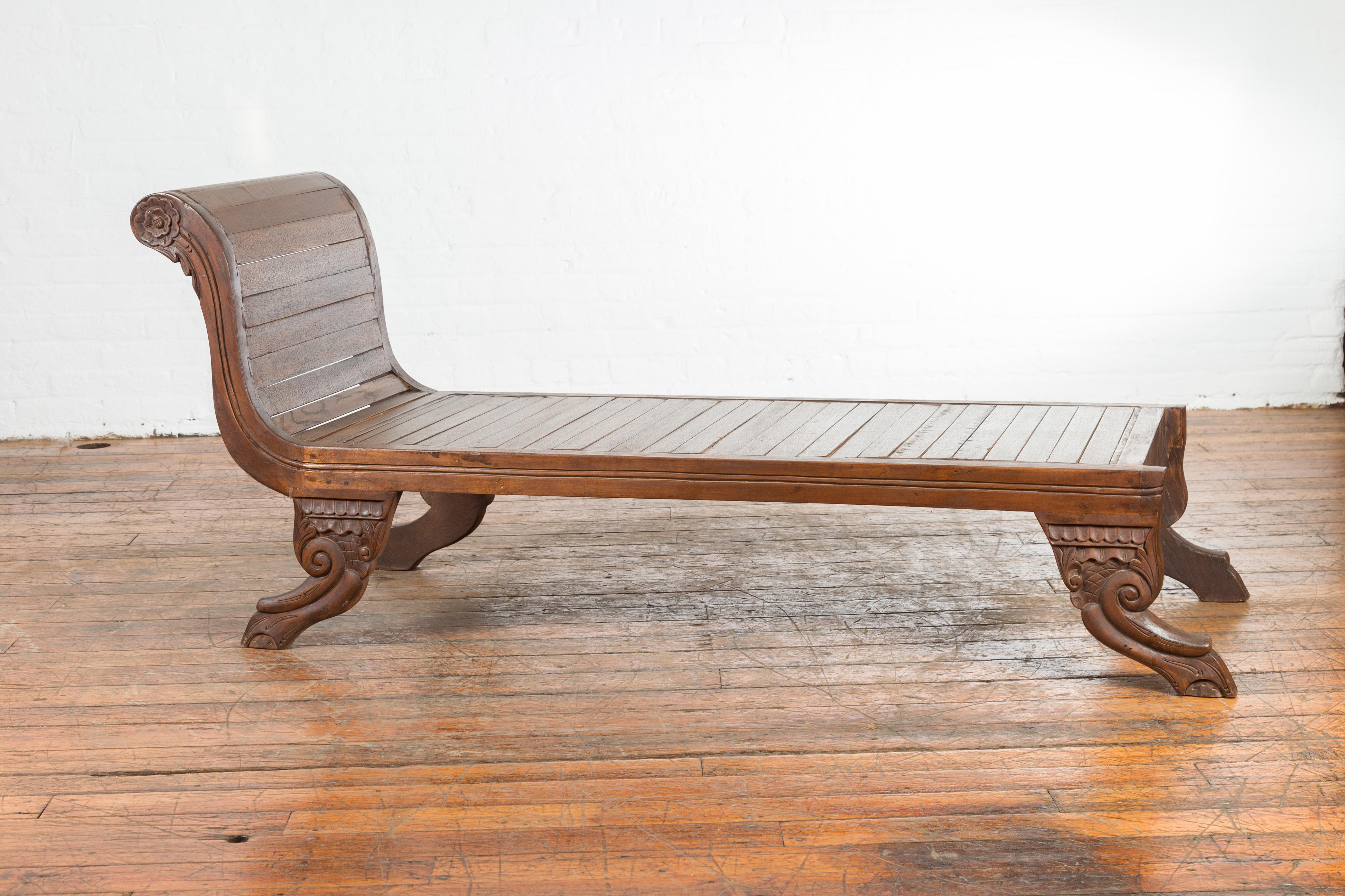 A Dutch Colonial period Indonesian lounge chair from the early 20th century with paw feet and slatted seat. Created in Indonesia during the early years of the 20th century, this wooden lounge chair features an out-scrolling back adorned with carved