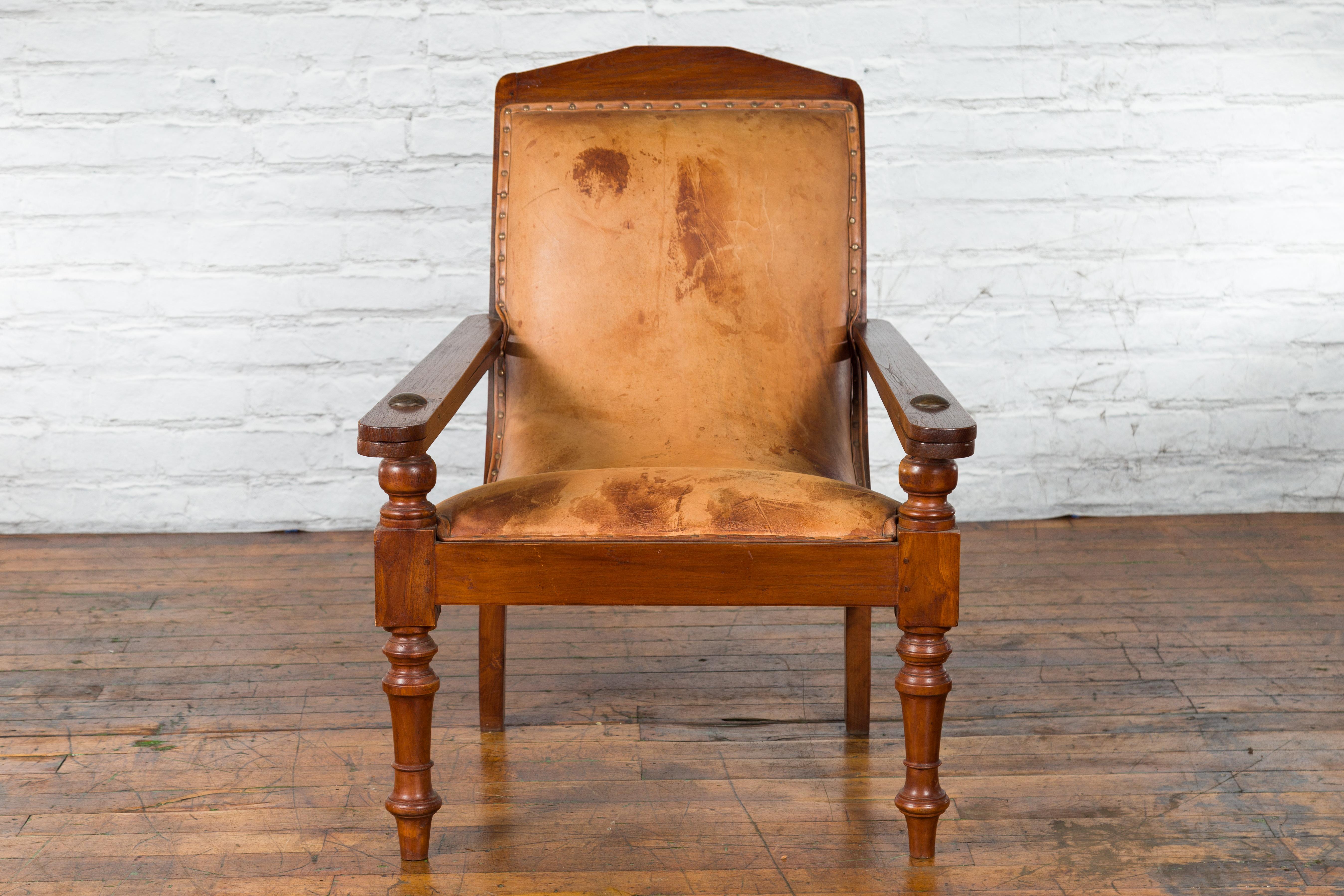 A Dutch Colonial period Indonesian wooden plantation lounge chair from the early 20th century with leather upholstery and nailhead trim. Created in Indonesia during the first half of the 20th century, this Dutch Colonial plantation chair features a