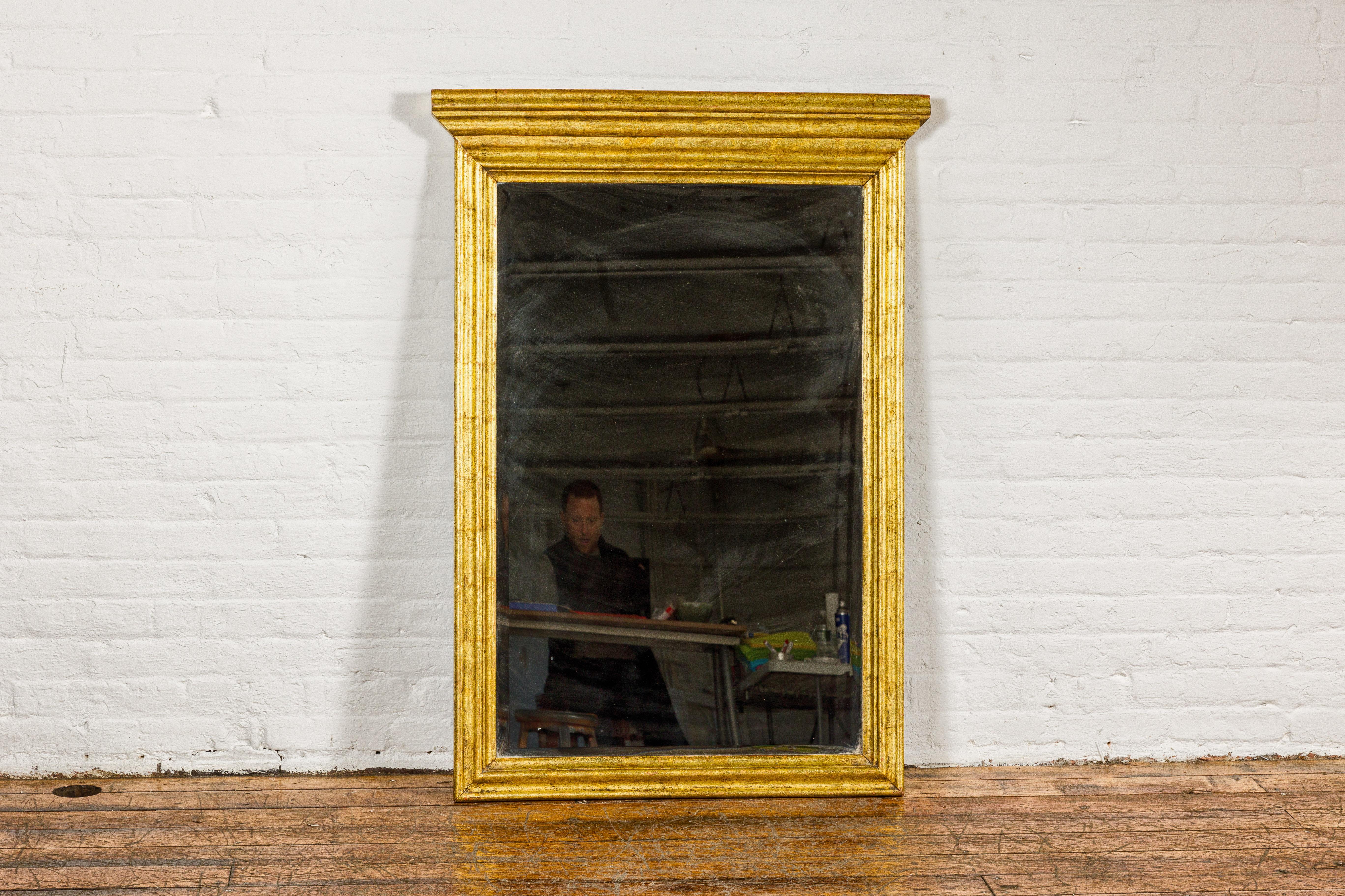 A Dutch Colonial gold leaf trumeau mirror with beveled glass and molded cornice. This Dutch Colonial trumeau mirror exudes an air of vintage elegance, with its radiant gold leaf frame offering a luxurious aura. The mirror itself boasts beveled