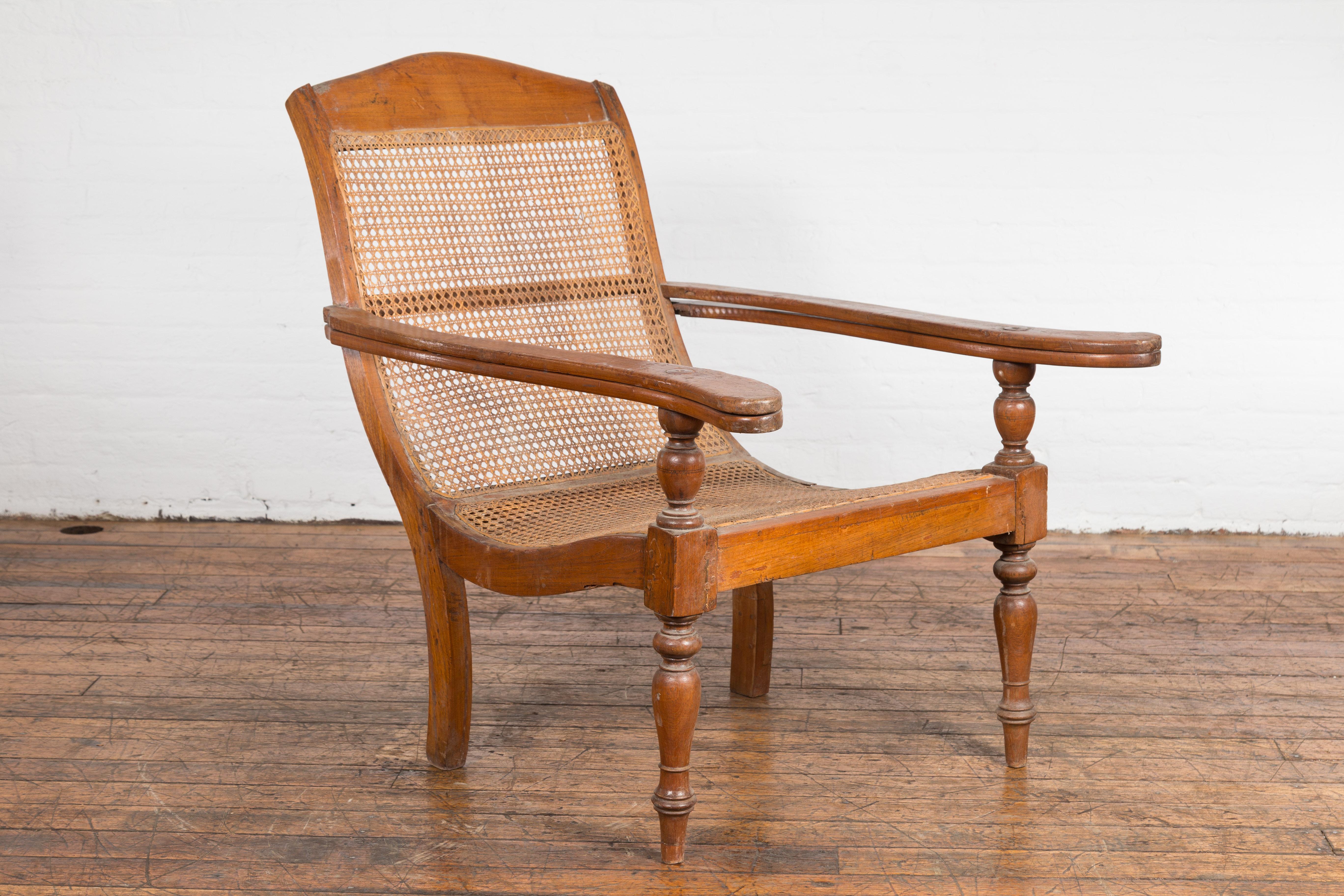 An antique Dutch Colonial Indonesian cane and wood plantation chair from the 20th century with extending arms and turned baluster legs. This antique Dutch Colonial Indonesian plantation chair from the 20th century is an exquisite blend of form and