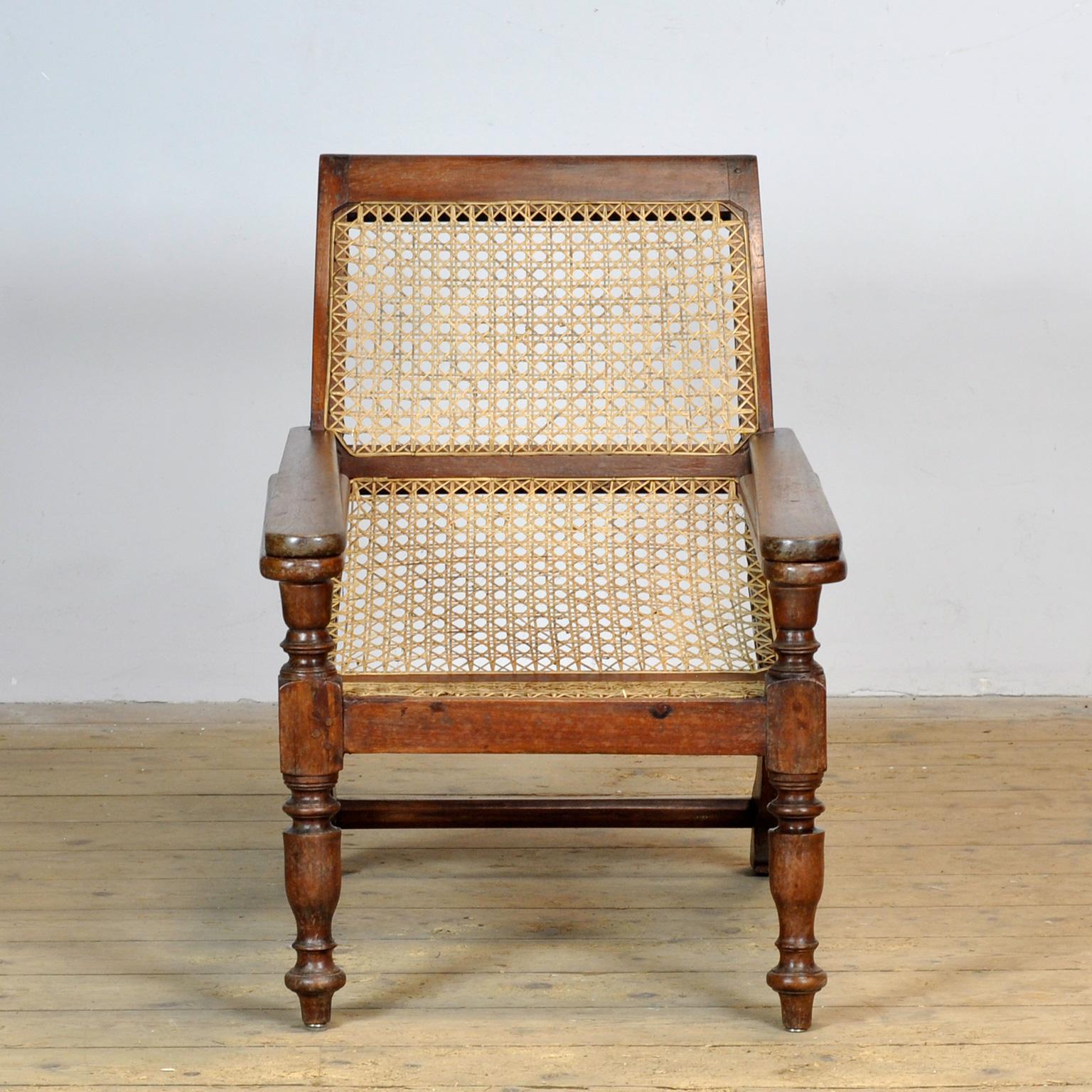 Silla de plantación de mimbre y madera indonesia colonial holandesa del siglo XX, con brazos extensibles y patas de balaustre torneadas. Fabricada en madera de teca y decorada con el tradicional tejido de mimbre, esta silla tiene brazos extensibles