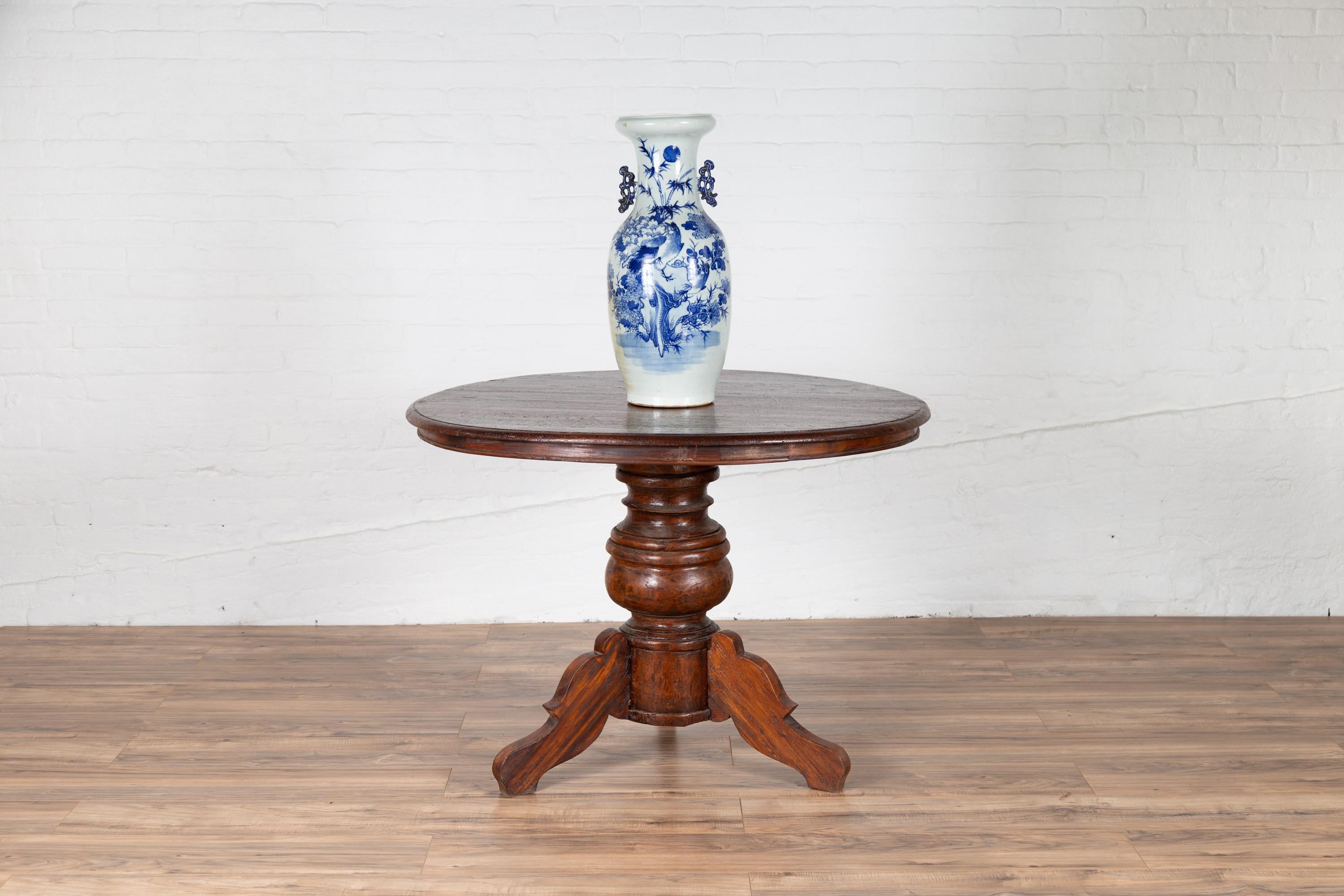 A Dutch Colonial Indonesian pedestal tripod table from the early 20th century, with circular top and turned base. Found in Java, this lovely pedestal table features a circular planked top sitting above a turned base, resting on three scrolling feet.