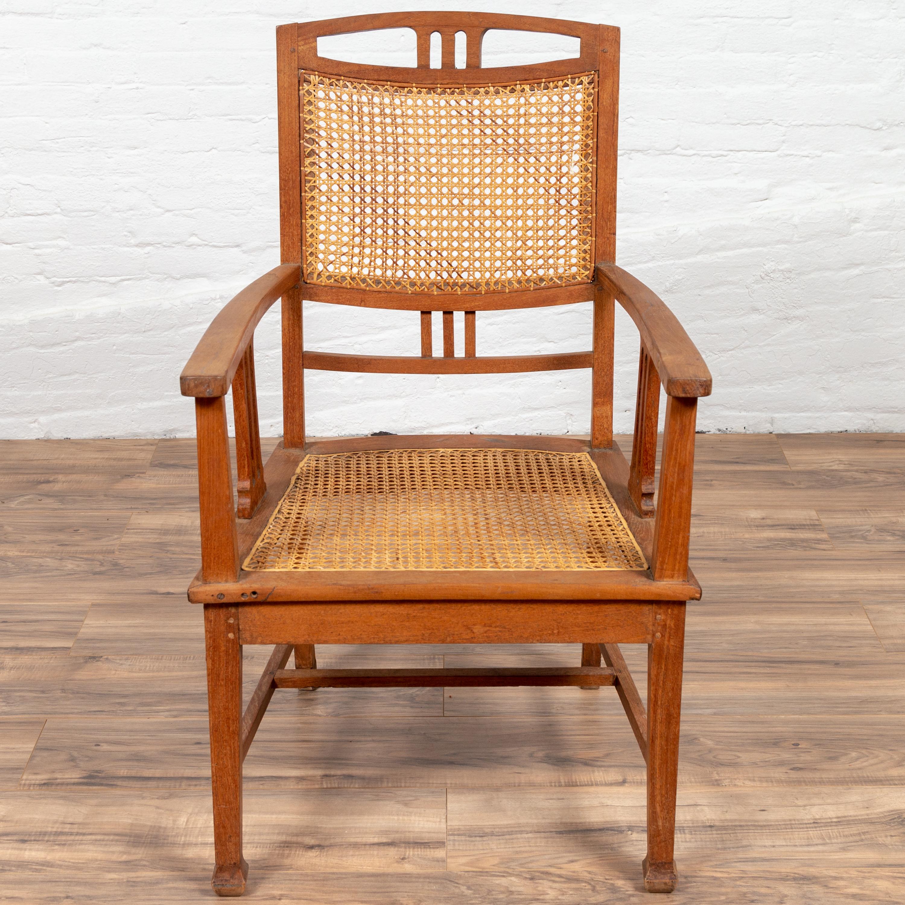 Antique Javanese Dutch colonial teak wood armchair from the early 20th century, with rattan seat and triglyph inspired motifs. Born on the island of Java during the early years of the 20th century, this elegant teak armchair features a slightly