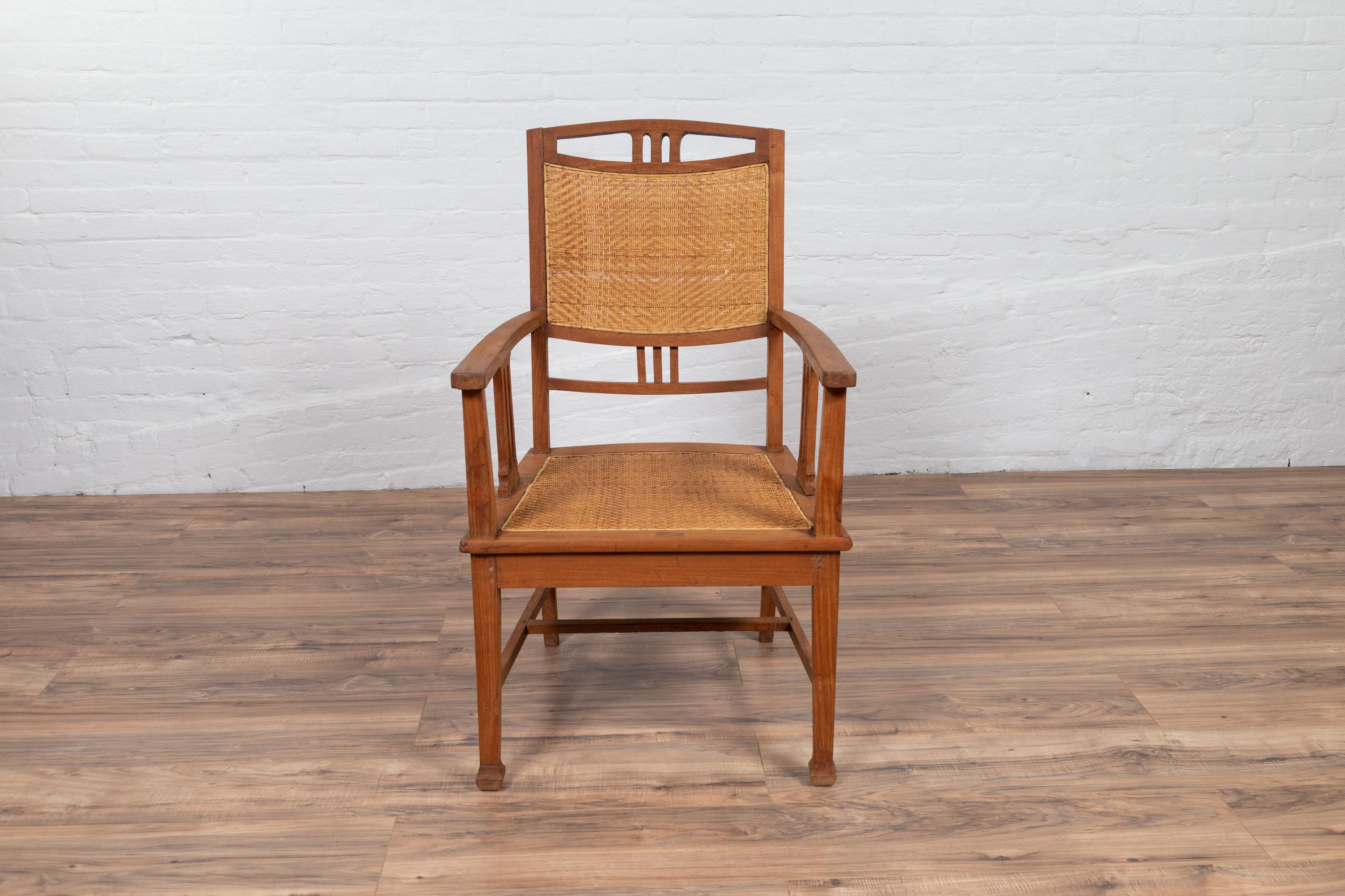 Antique Javanese Dutch colonial teak wood armchair from the early 20th century, with rattan seat and triglyph inspired motifs. We currently have two available, priced and sold individually. Born on the island of Java during the early years of the