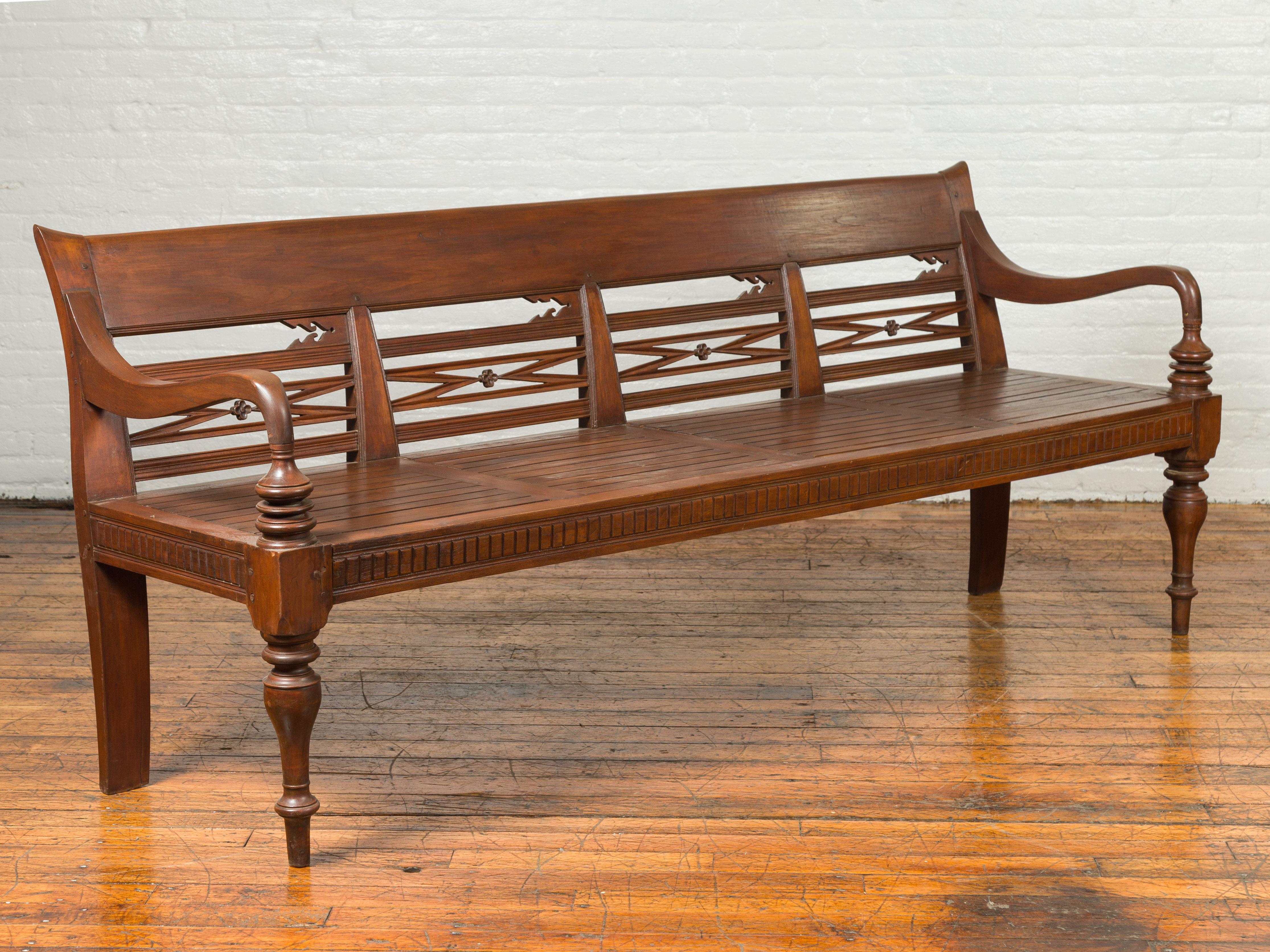 A Dutch Colonial Indonesian wooden garden bench from the 19th century, with pierced back, floral motifs and scrolling arms. Crafted in Indonesia during the later years of the 19th century, this Dutch Colonial bench features a slanted back pierced