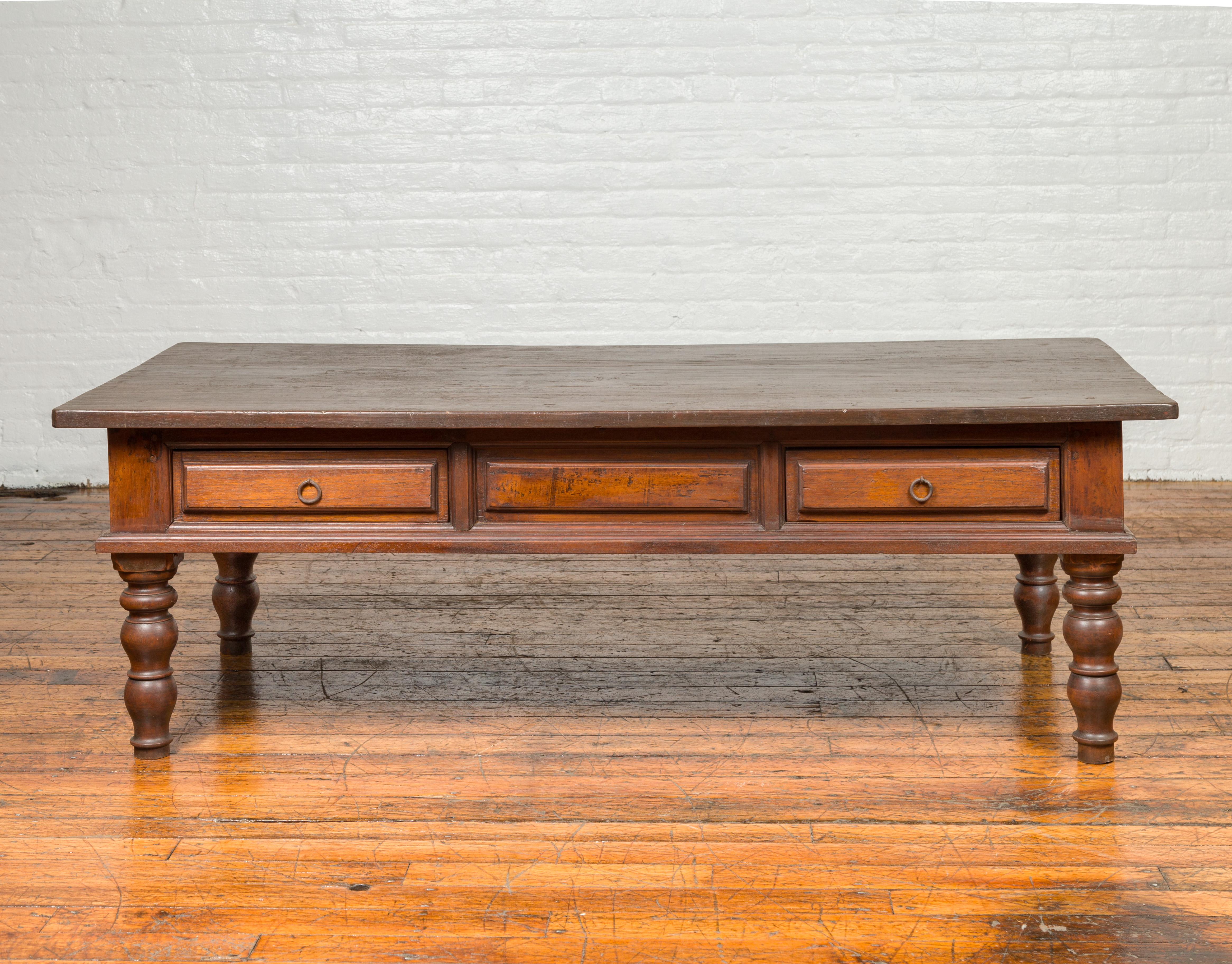 A long Dutch Colonial antique coffee table from the 19th century, with two drawers and turned legs. Crafted in Indonesia during the later years of the 19th century, this Dutch Colonial coffee table features a rectangular planked top resting above