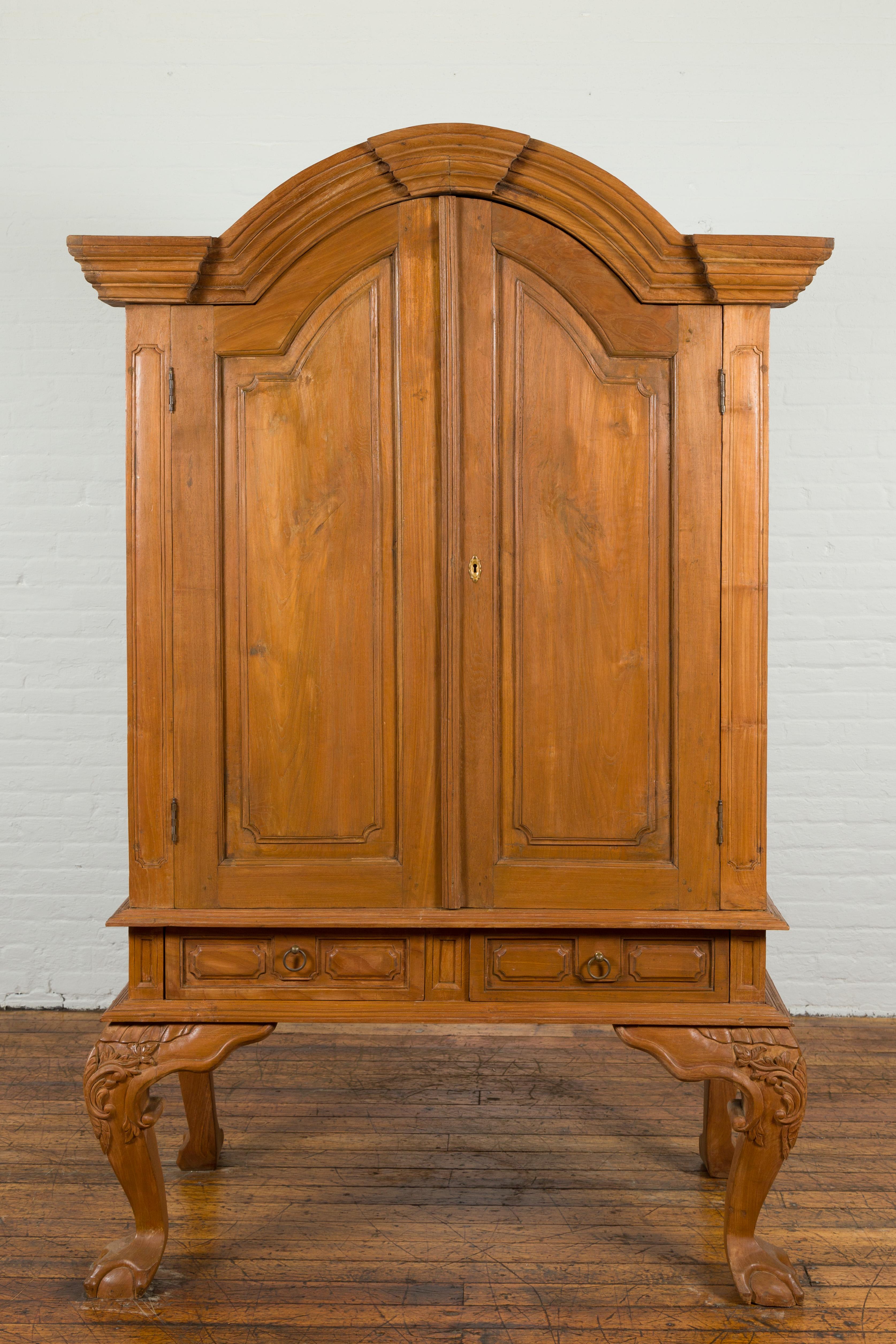 A Dutch Colonial period Indonesian teak cabinet from the late 19th century, with bonnet top, two drawers, cabriole legs and ball and claw feet. Created in Indonesia during the Dutch Colonial era, this teak cabinet features a molded bonnet top