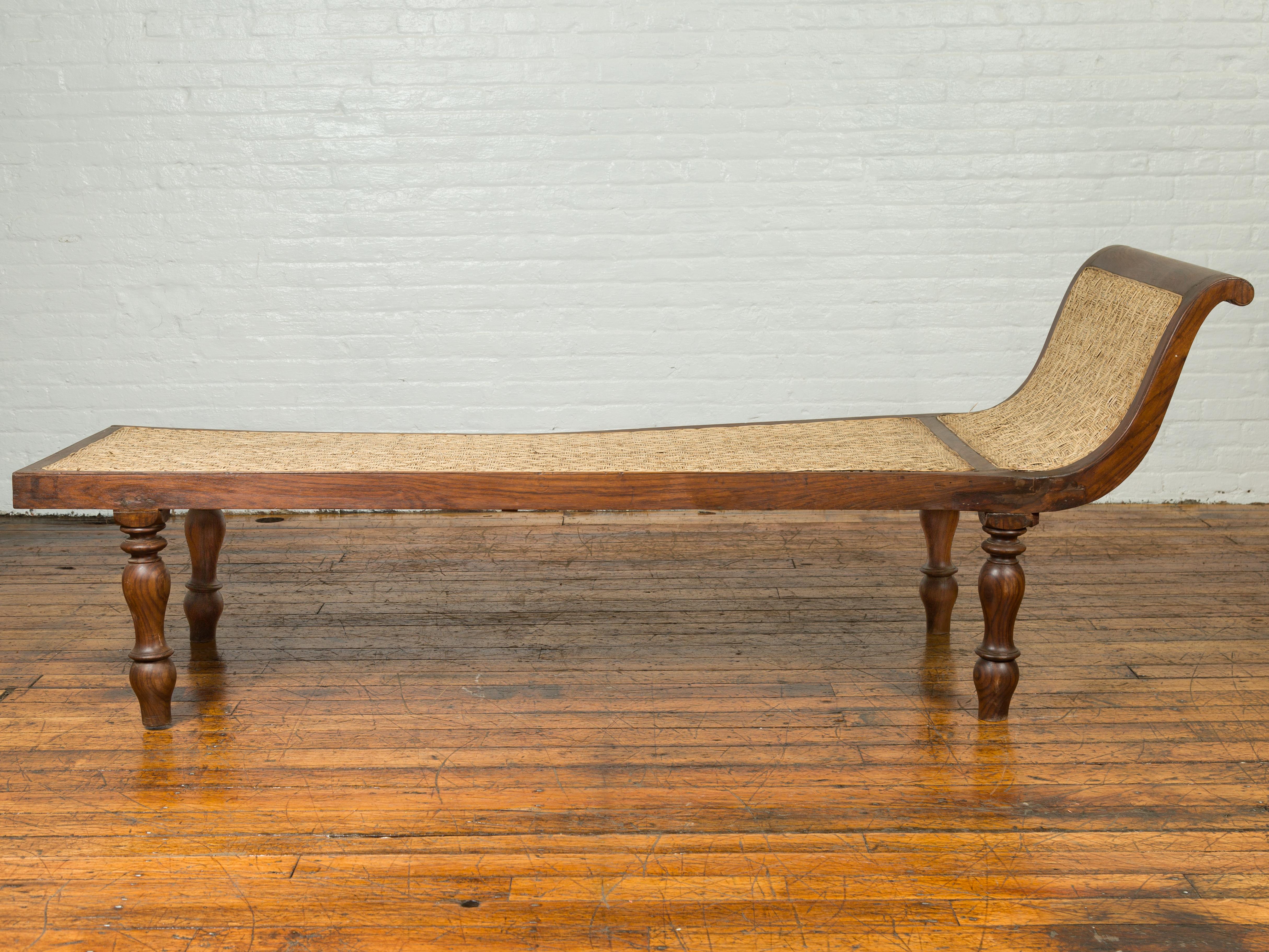 A Dutch Colonial Indonesian teak wood daybed from the late 19th century, with rattan seat and turned legs. Found in Jakarta, this Dutch Colonial daybed features an out-scrolling back, flowing seamlessly into the long rectangular seat. Covered with