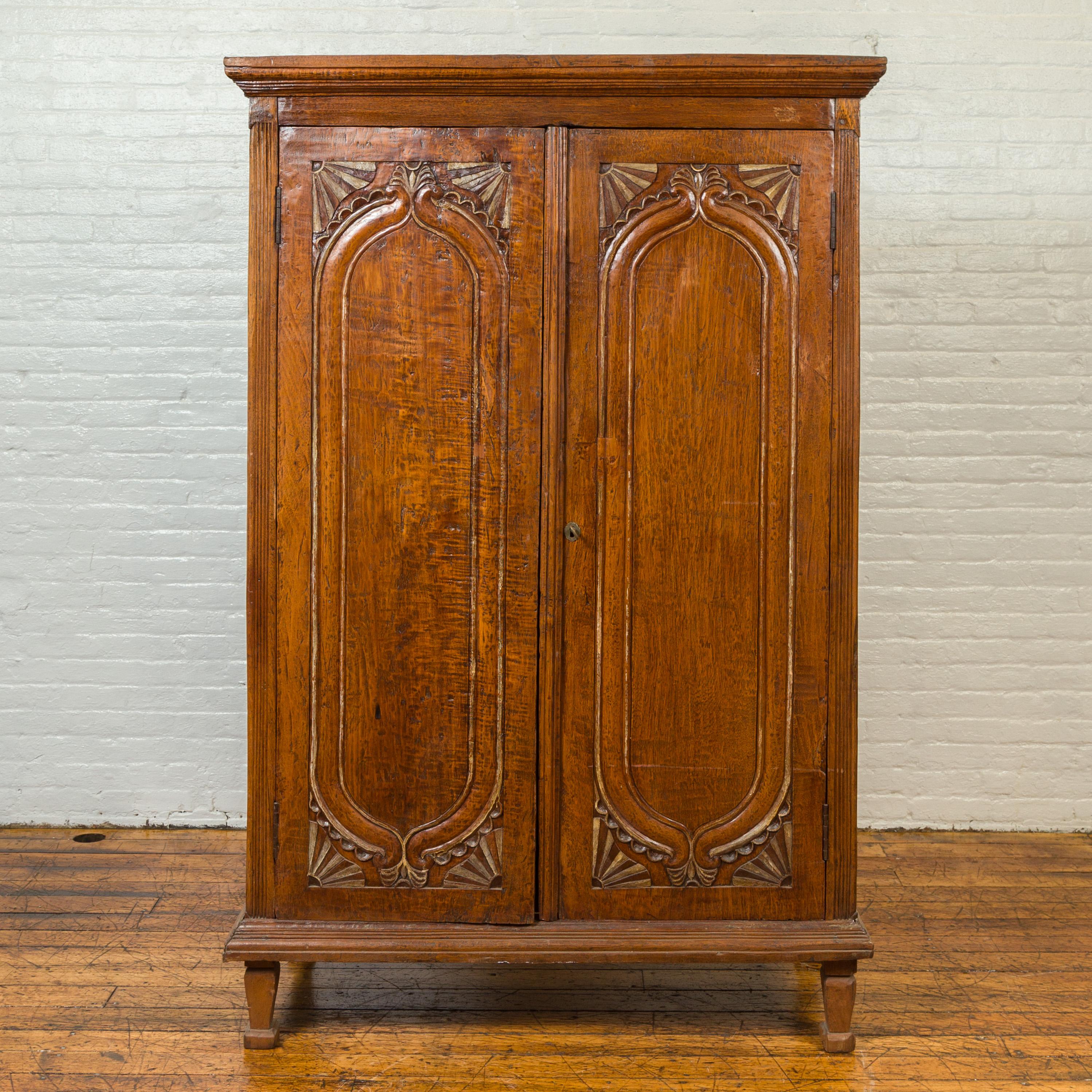 A Dutch Colonial period antique Indonesian teak wood cabinet from the late 19th century, with carved fan motifs. Crafted during the later years of the 19th century, this teak wood cabinet features a molded cornice overhanging two large doors,