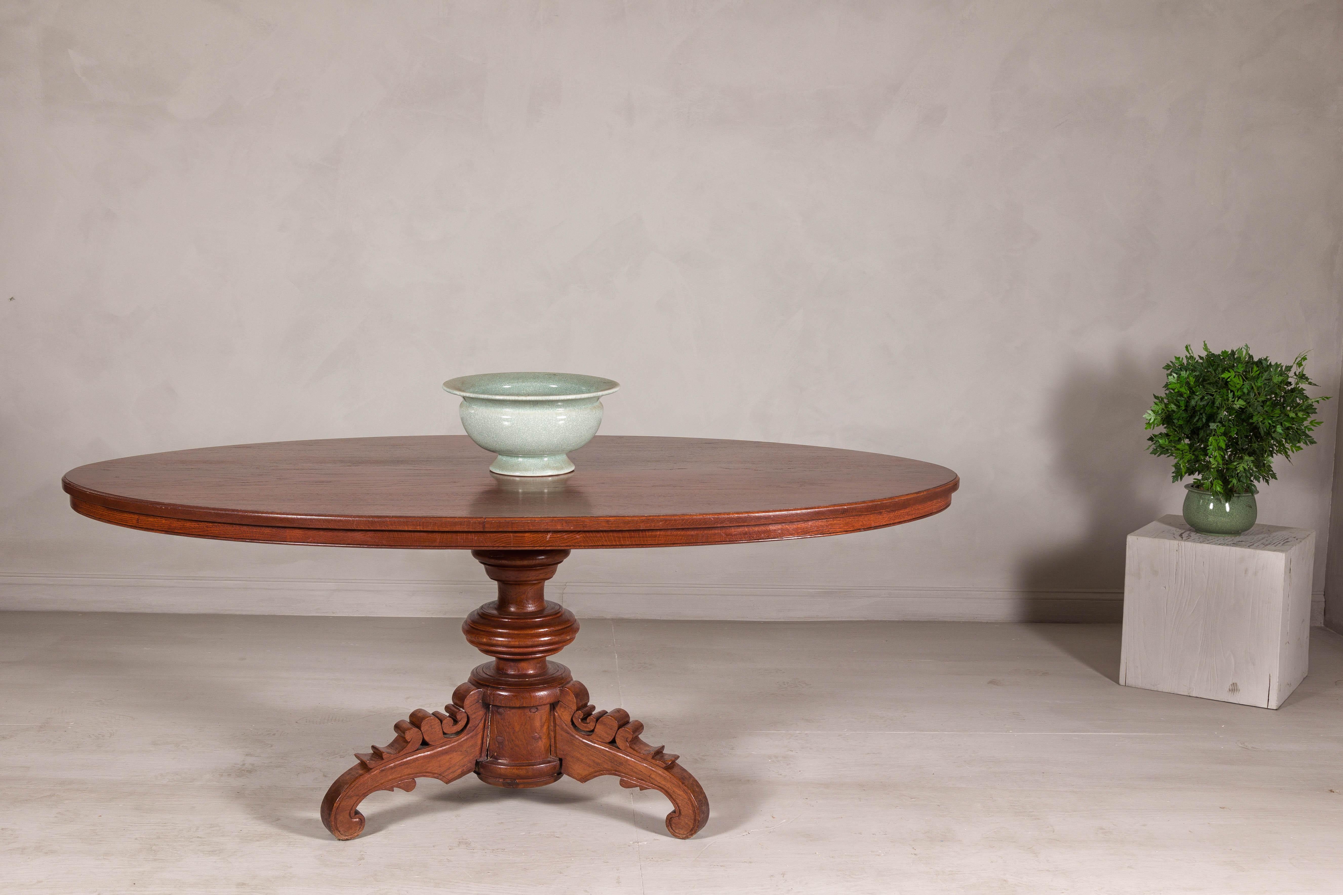 A Dutch Colonial oval top dining table from the late 19th century with scrolled pedestal base. This late 19th-century Dutch Colonial oval pedestal dining table brings classic charm and timeless craftsmanship to any dining room. Its generous