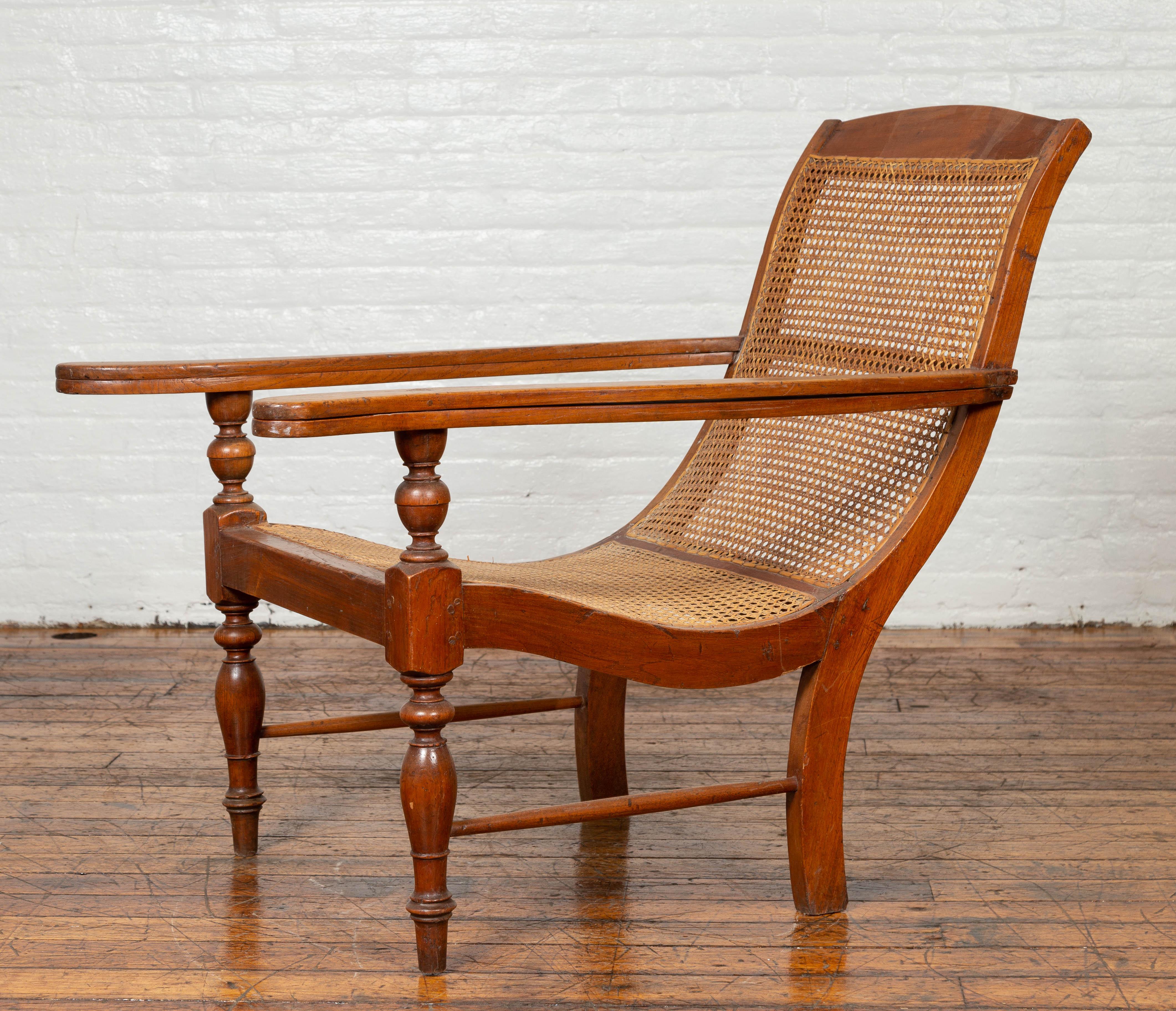 A vintage Dutch Colonial Indonesian teak wood plantation lounge chair from the mid-20th century, with rattan and extending arms. Designed to provide a relaxing experience to the sitter, this Dutch Colonial lounge chair features a nicely curving body