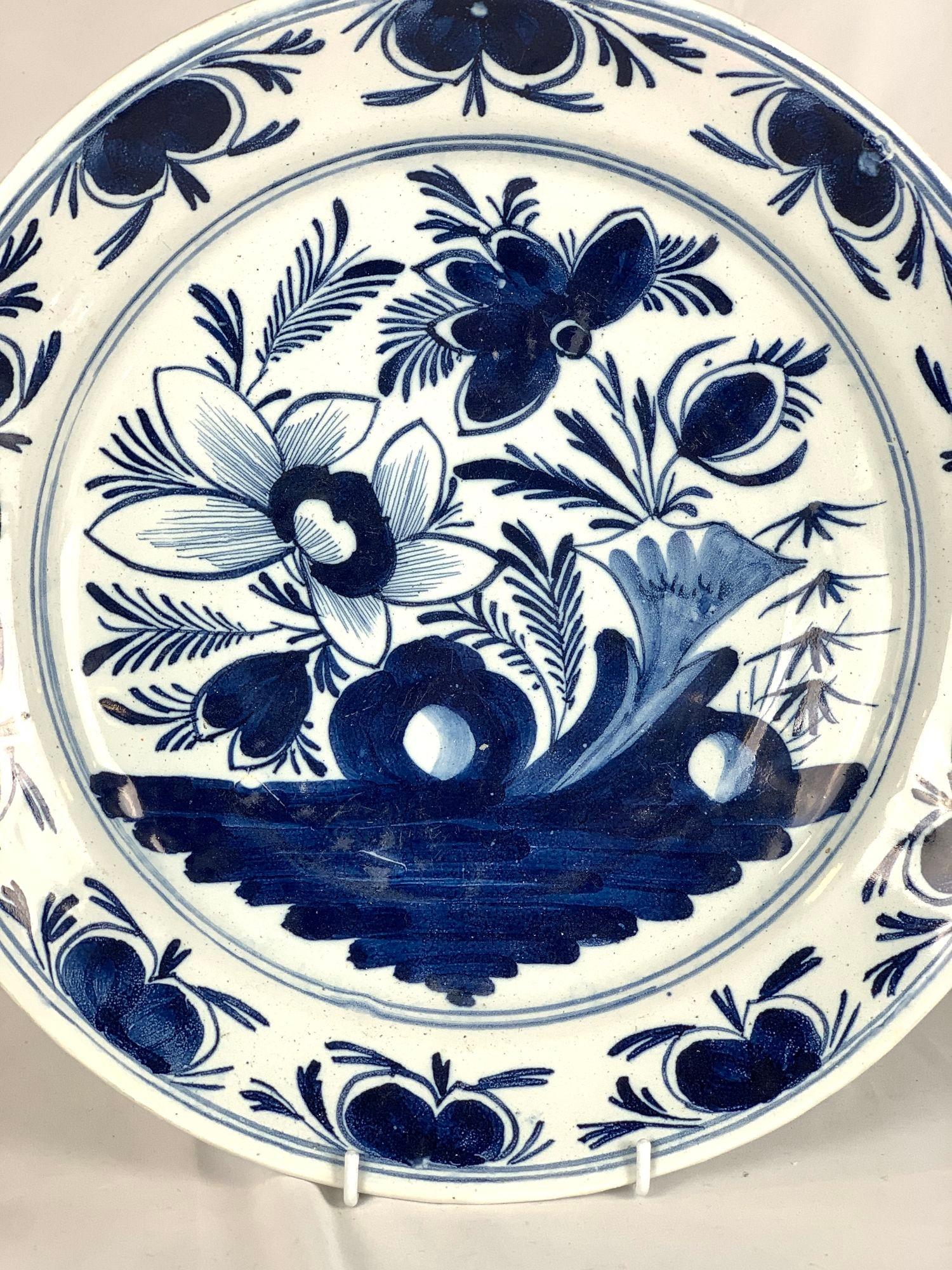 Hand painted in the Netherlands circa 1800, this blue and white Delft charger features a garden scene with flowering peonies.
We see blossoming flowers, buds, leaves, and rockwork.
The wide border shows a lovely repeating motif of buds and
