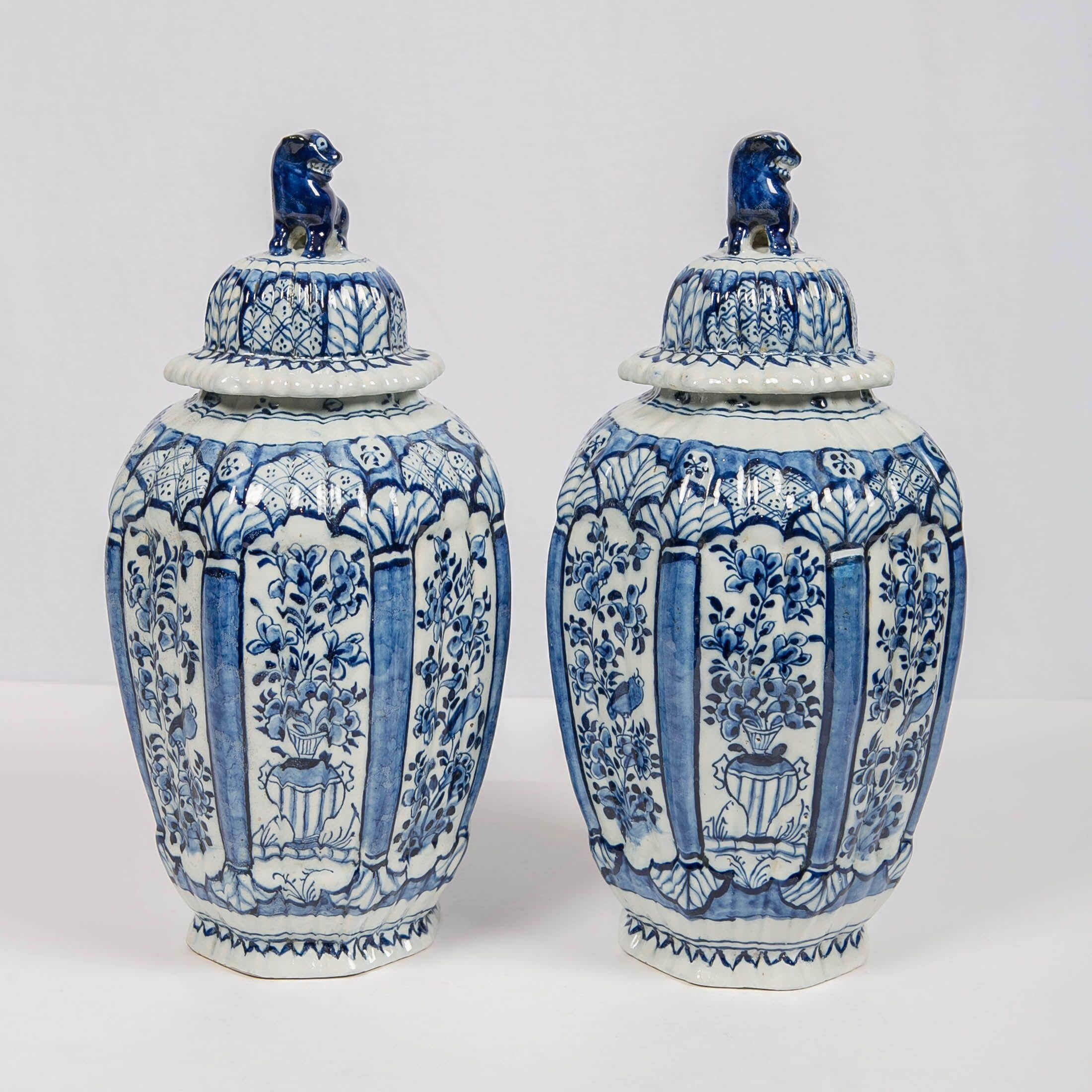 We are pleased to offer this beautiful pair of Dutch delft blue and white ginger jars with lion finials. They are molded in the traditional delft octagonal shape with a fluted surface. The jars are decorated with panels showing a songbird in a