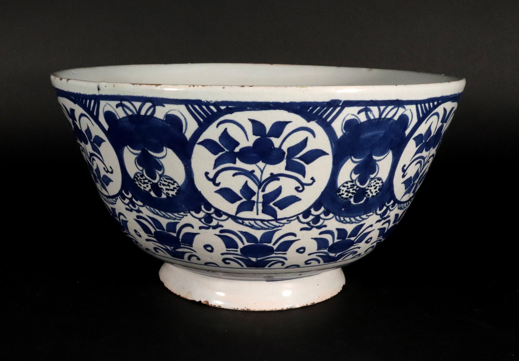 Cuenco Botánico Azul y Blanco de Delft Holandés,
Alrededor de 1720

Este cuenco alto de cerámica holandesa de Delft, de color azul y blanco y pie liso acampanado, está pintado con una banda bajo el borde de seis grandes paneles circulares con una