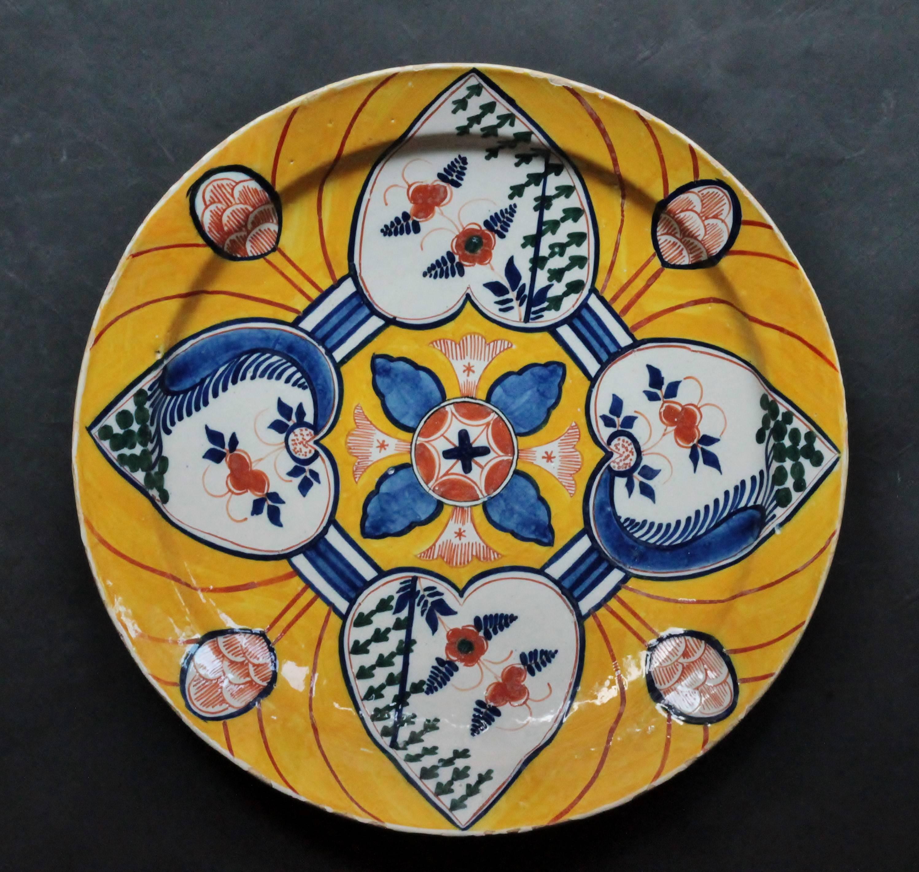 A Dutch Delft faience dish with a colors decoration says “four hearts” on a yellow background.
Undetermined mark in blue at the back. First half of the 18th century. Measures: D 36 cm., H 5.3 cm
A little piece restored on the rim and some minor