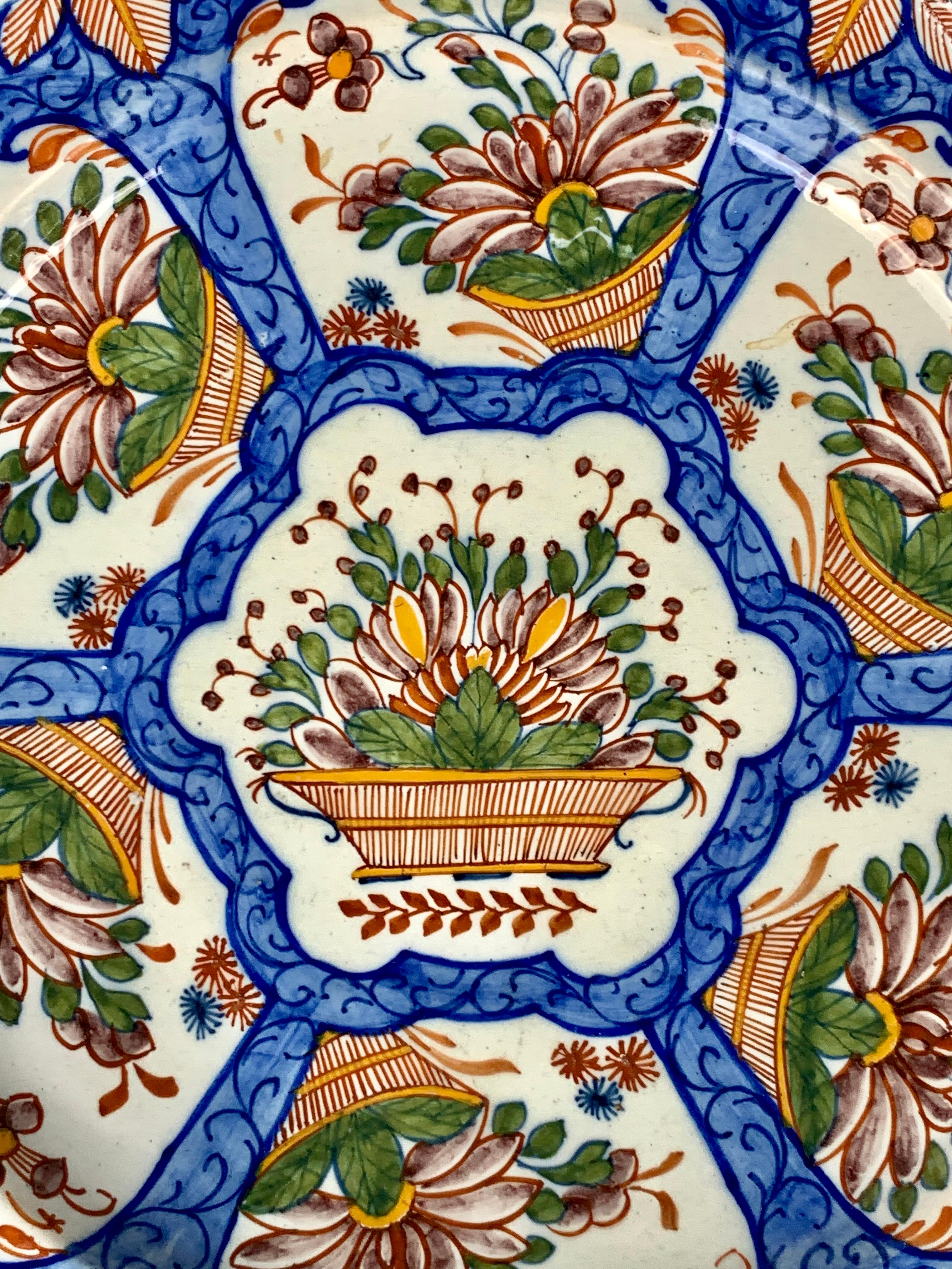 A Dutch Delft charger hand-painted in colorful polychrome. Made in the mid-18th century, the charger shows a traditional Dutch Delft design of a beautiful overflowing flower basket in panels. The panels are separated by an exquisite medium blue