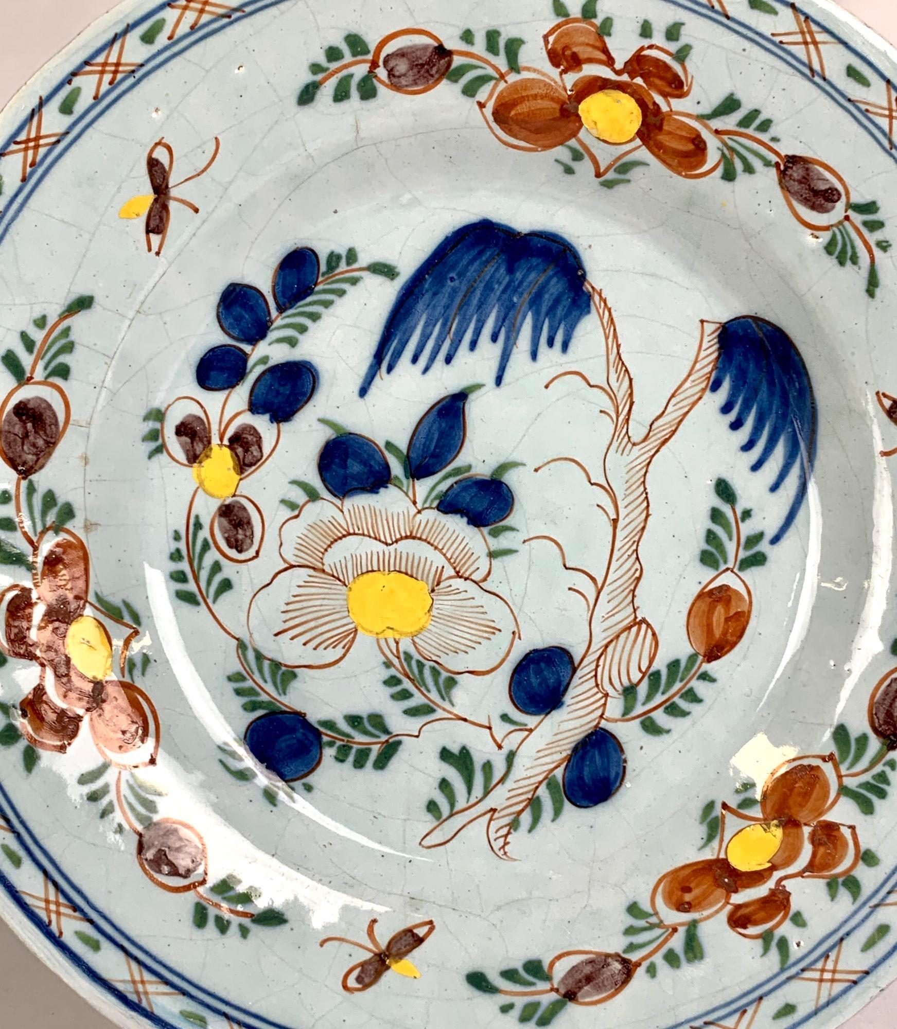 The center of this hand painted Dutch Delft plate shows a lovely garden with a pine tree and a large peony.
The scene continues onto the border, where we see three butterflies and more peonies.
The border is decorated with a band of iron red