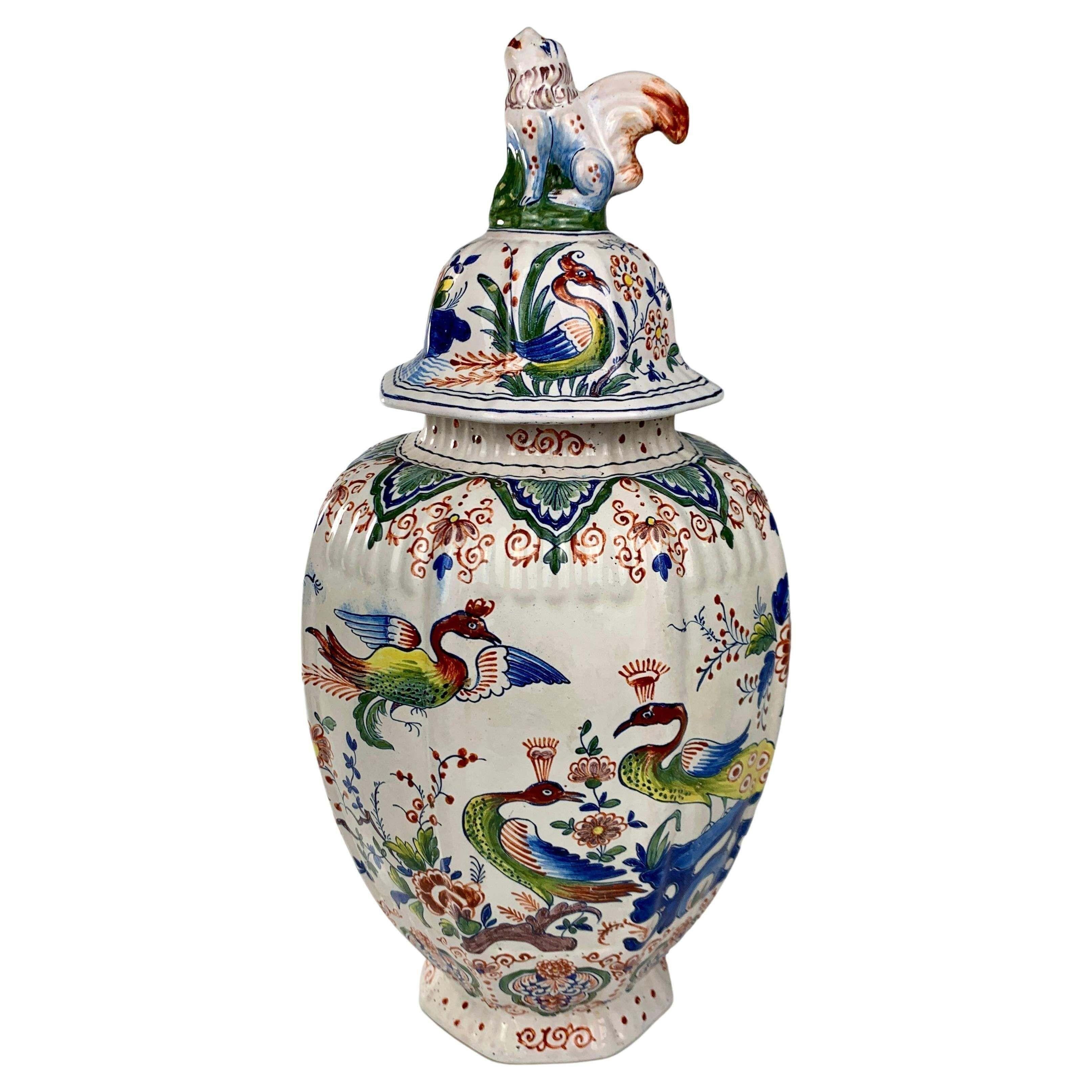 This Dutch Delft jar is hand-painted in the traditional Delft polychrome colors of iron-red, manganese, moss green, cobalt blue, and accents of bright yellow. We see a lush garden with peacocks and stylized flowers in full bloom.
The jar is shaped