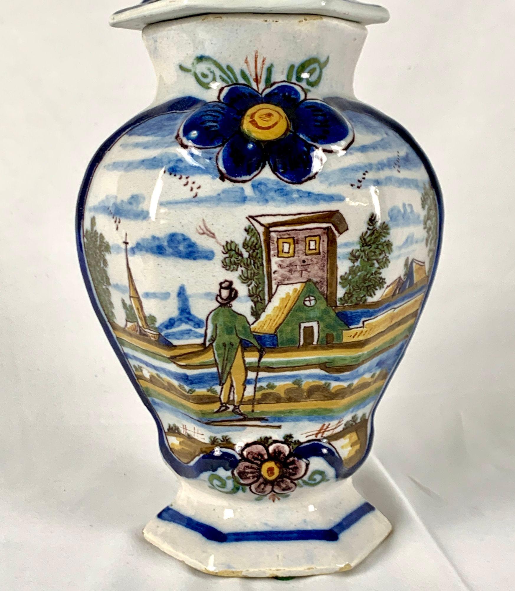 This lovely 18th century Delft jar was made in the factory of De Bloempot in Delft, The Netherlands, circa 1780.
The design features a gentleman with a top hat and a walking stick standing at the side of a river.
He looks across at the buildings of