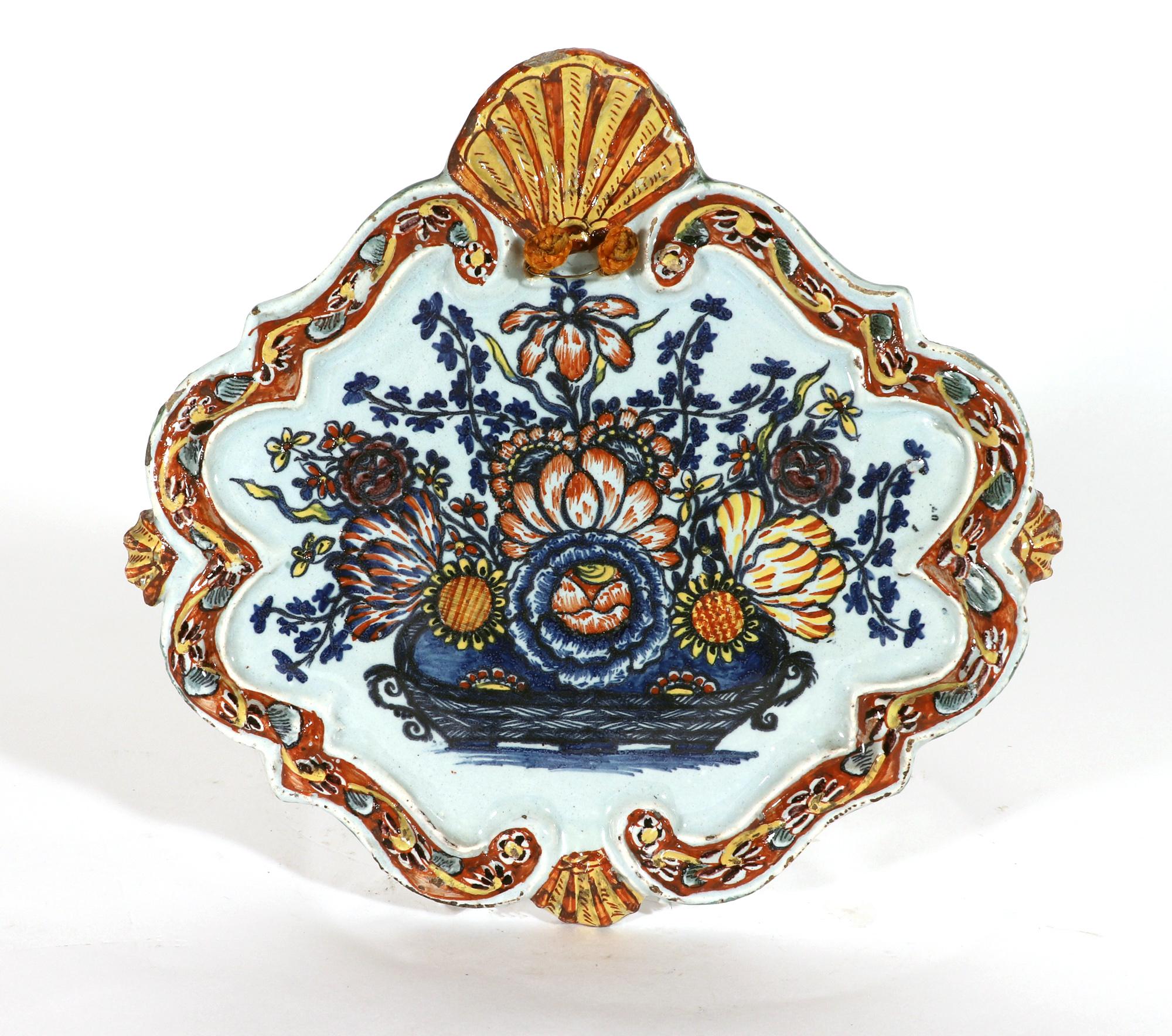 Dutch Delft Polychrome Shaped Plaques,
A Pair,
Mid-18th century

The shaped Dutch Delft plaques each depict an exuberant display of flowers in an oval handled jardiniere. The molded, raised rim with a band of red with a continuous floral vine in