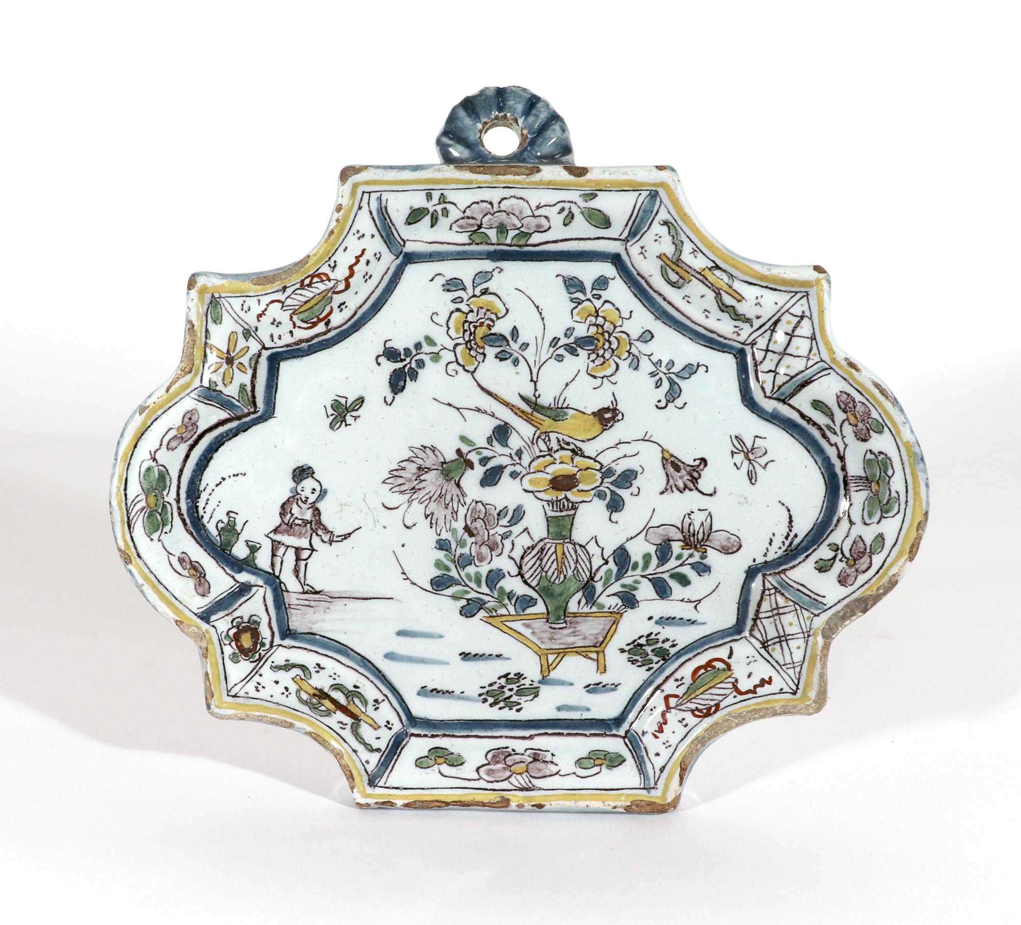 Dutch Delft shaped Chinoiserie Polychrome plaque,
Circa 1730-40

The shaped plaque has a raised molded border decorated with a series of alternating painted panels of flowers and Chinese auspicious objects. The central scene is painted with a