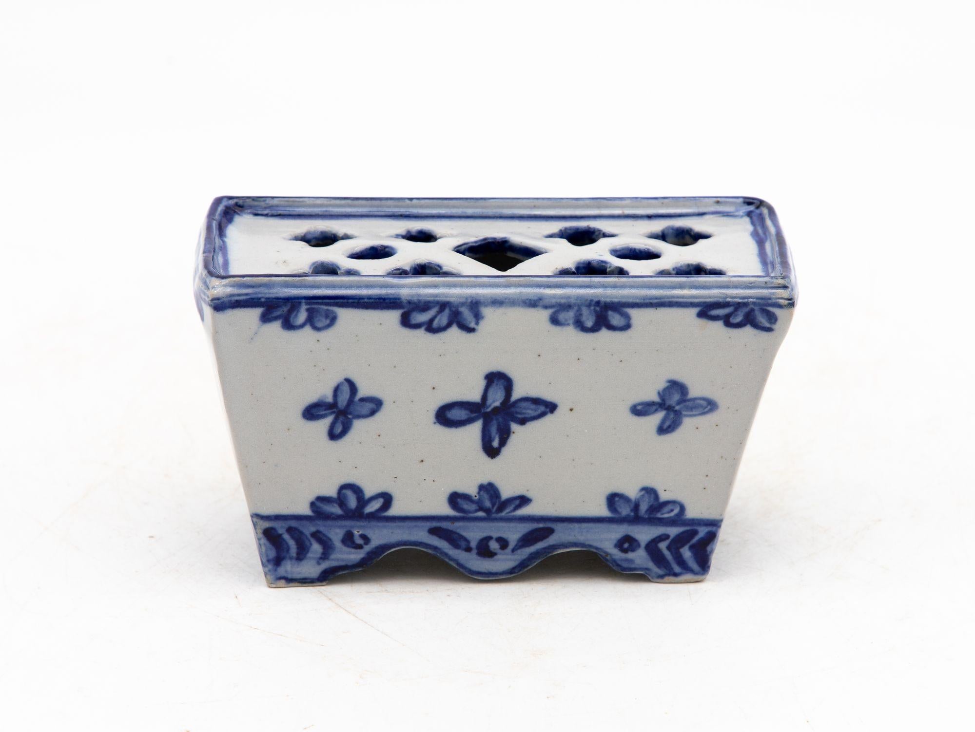 Una piccola rana o mattone di fiori in porcellana blu e bianca in stile Delft olandese con piede smerlato e profilo trapezoidale. I lati presentano un motivo floreale ripetuto e dipinto a mano, mentre la parte superiore forata accoglie ordinatamente