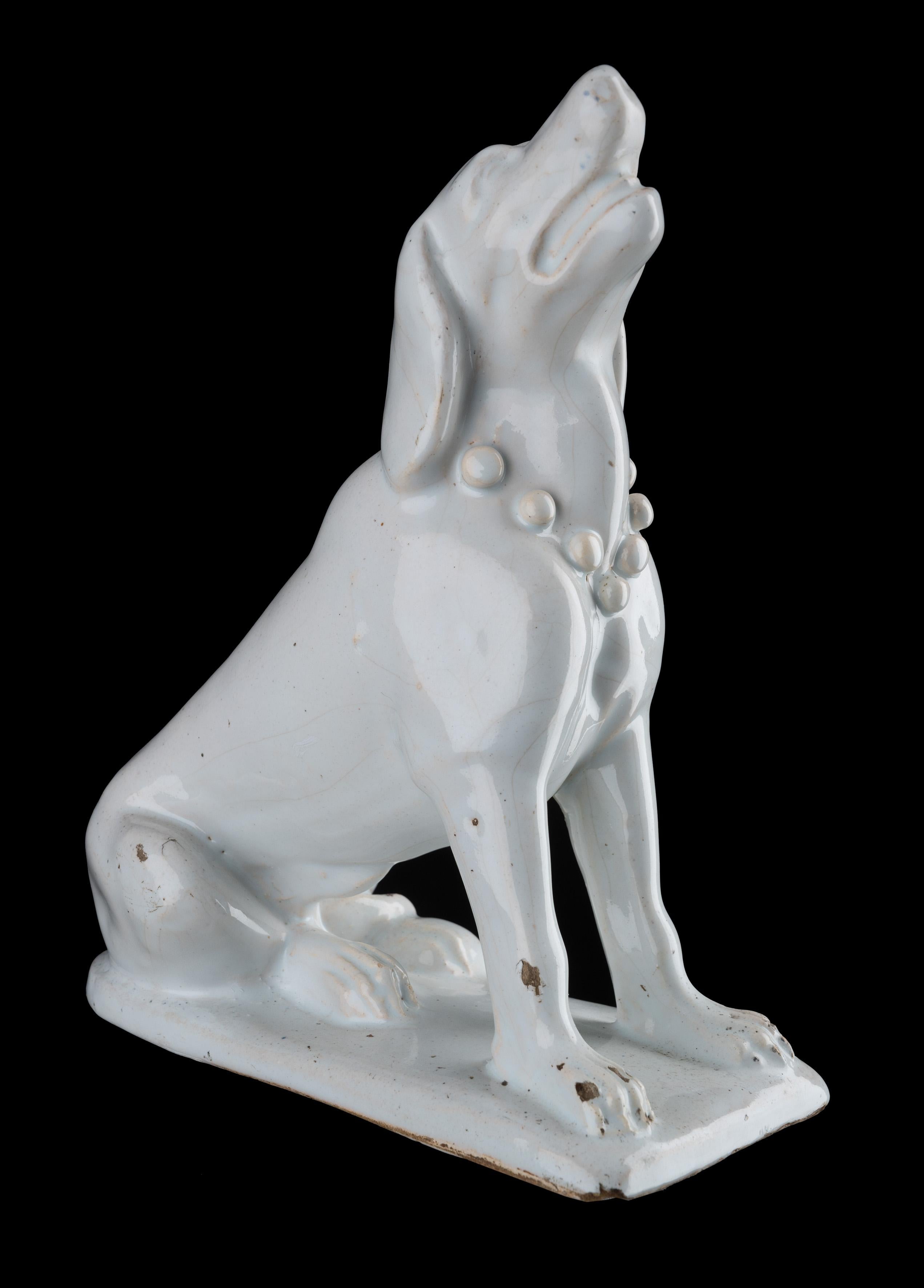 Dutch delftware A sitting dog. Delft, 1725-1775

The moulded dog is sitting on a rectangular plinth with rounded back and has its head raised and its snout opened. Around its neck is a collar with bulbs/spheres. The white-glazed dog is unpainted.