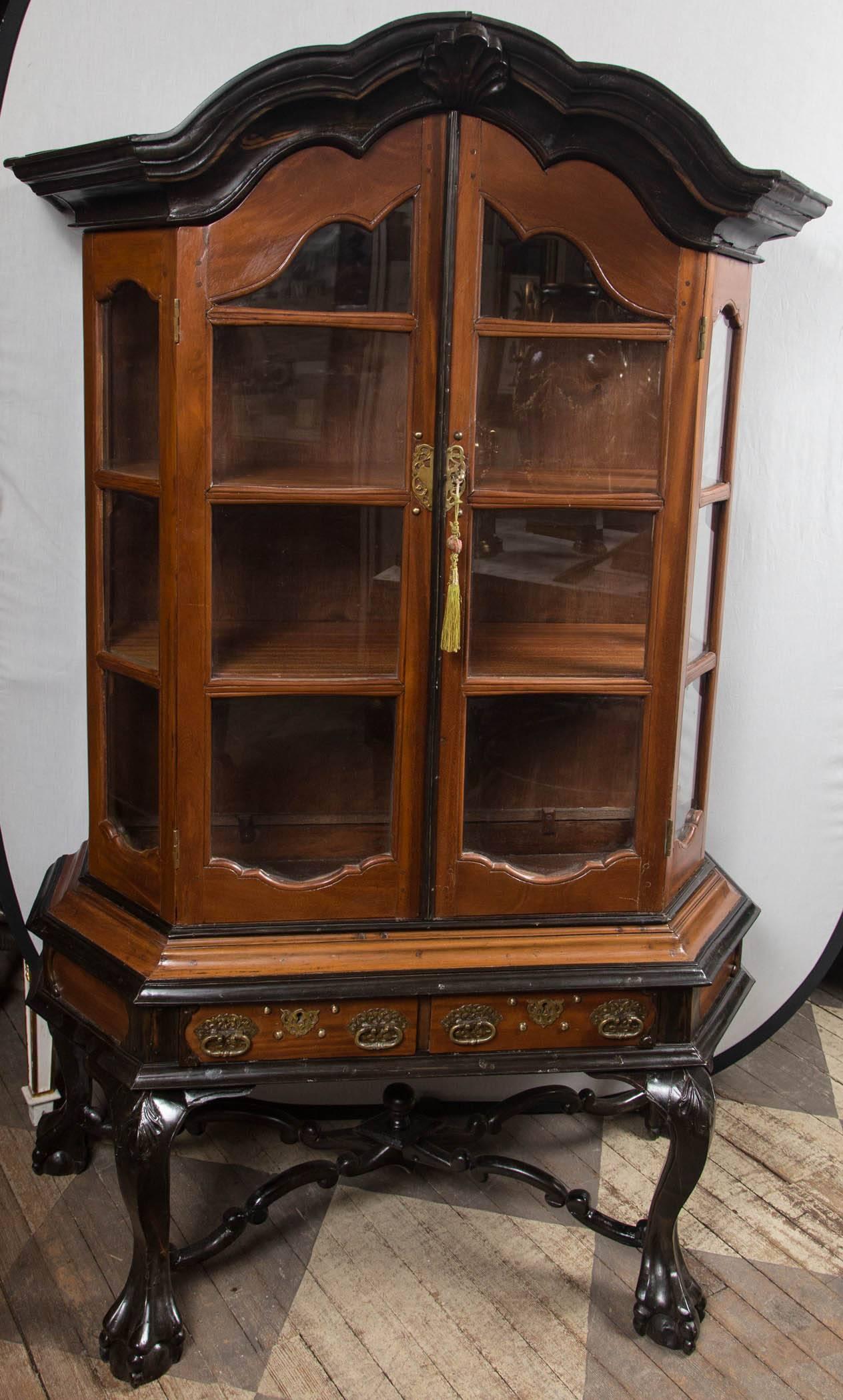 Double glazed doors with canted side glazed panes. Arched ebonized cornice, conforming door and side frames. Two shelves within. Two drawers below doors.
Ebonized base, ball and claw feet, cabriole legs joined by a stylized X-stretcher with
