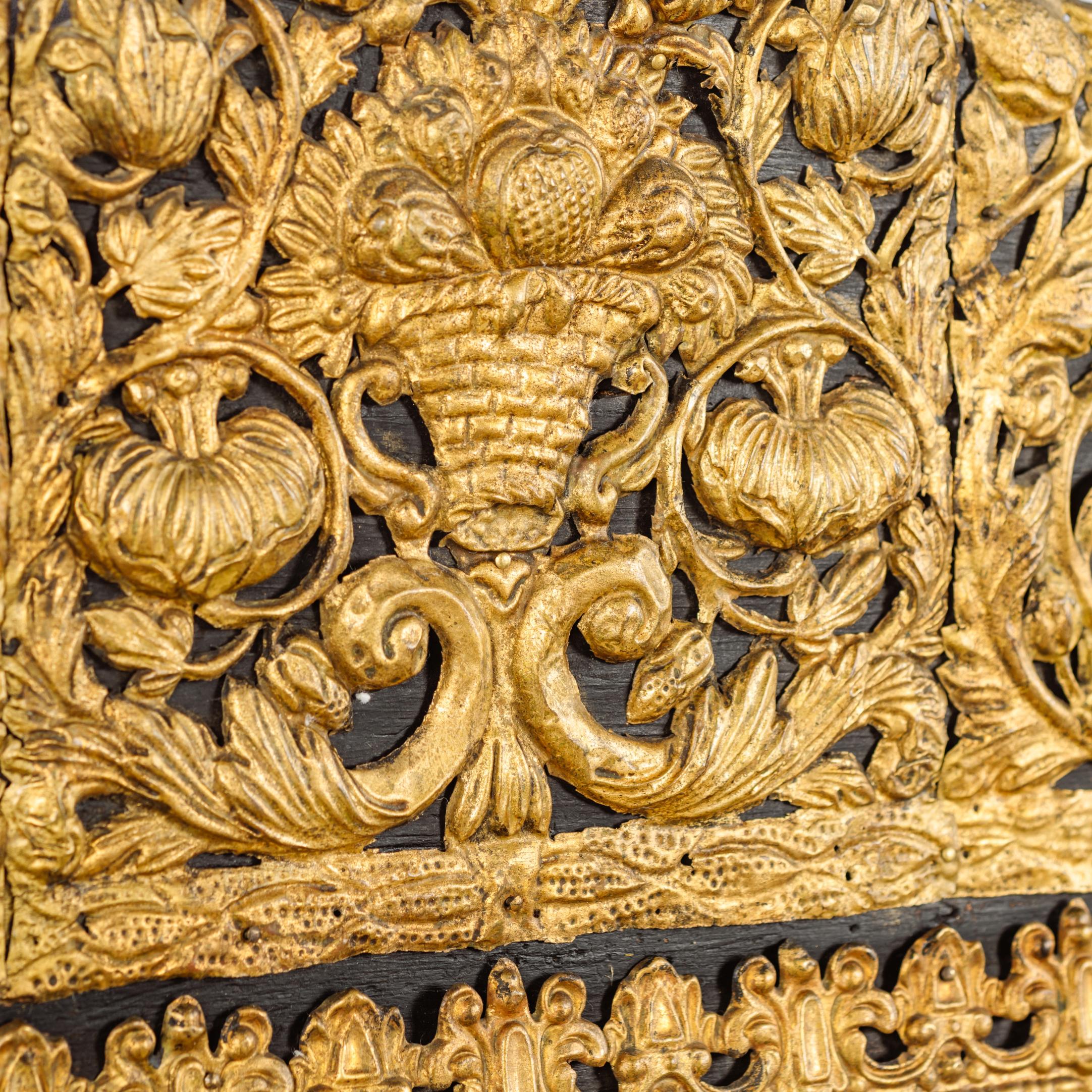A fine Dutch ebonized and repousse gilt-metal cushion mirror.

The rectangular beveled mirror plate with ebonized frame and marginal borders, surmounted by an arched cresting headed by a basket issuing fruit, applied overall with repousse worked