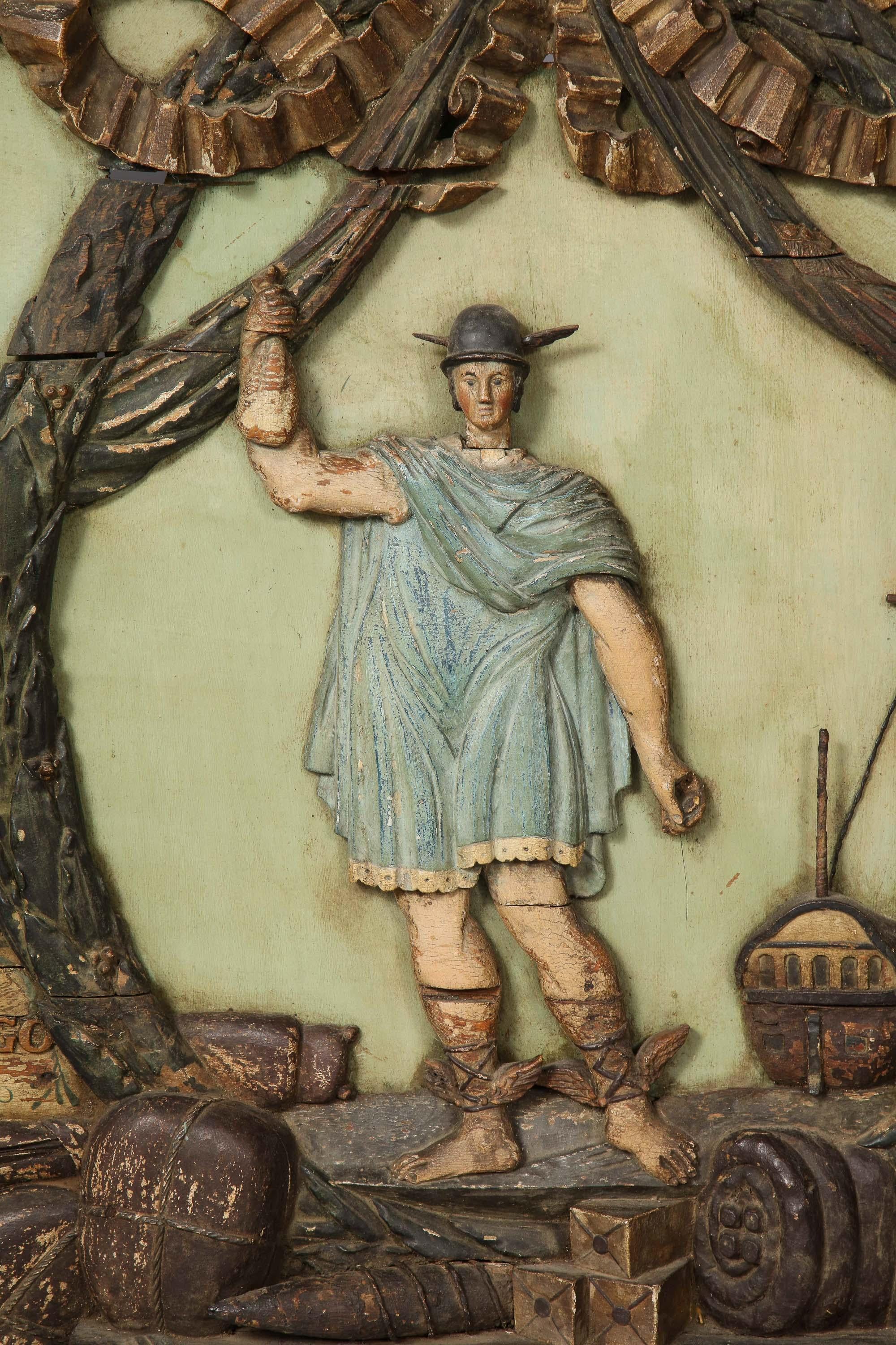 An 18th century trade sign from a Dutch West Indies shipping merchant. The carved and polychromed sign depicts a winged-foot mercury surrounded by garlands with his ship and the wares of tobacco merchant at his feet. This trade sign would function