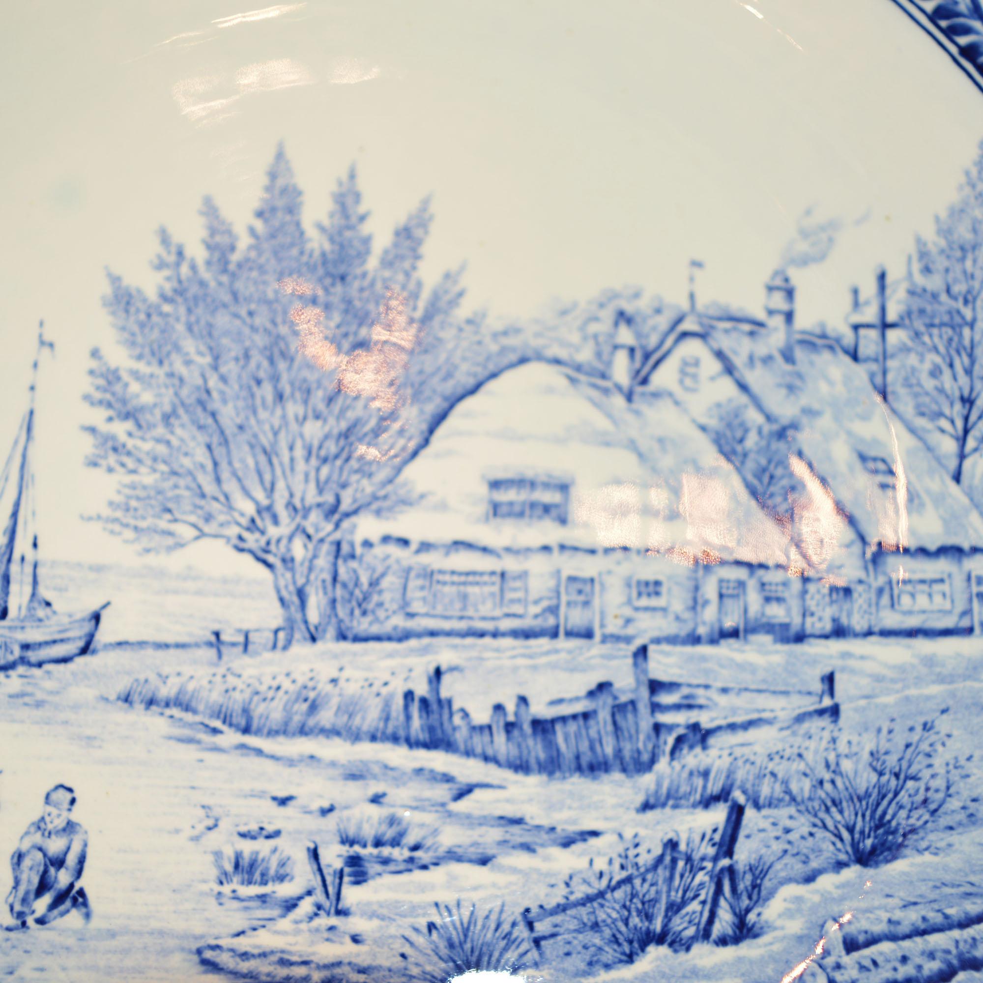 This large delft , blue and white charger/platter with intricately painted scene was made in Holland. The large wall hanging plate depicts a winding, frozen stream with a traditional Dutch windmill in the Classic blue and white palette. The scene