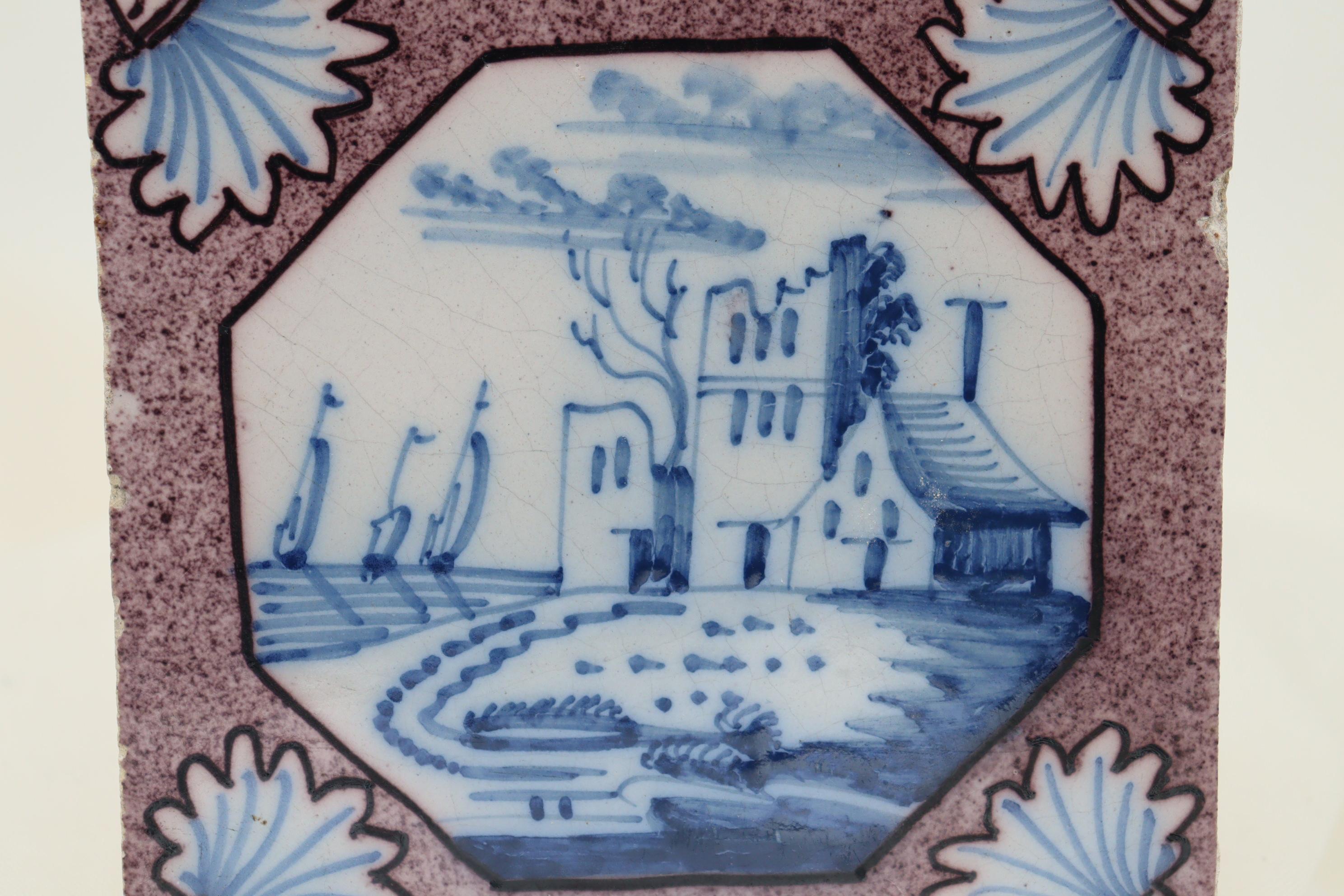 Die zentrale Dekoration auf dieser holländischen Fliese ist eine handgemalte Szene eines großen Hauses mit drei Schiffen im Hintergrund, alles in Blau auf der weißen Fliese. Die achteckige Kartusche ist von einem gesprenkelten violetten Grund mit