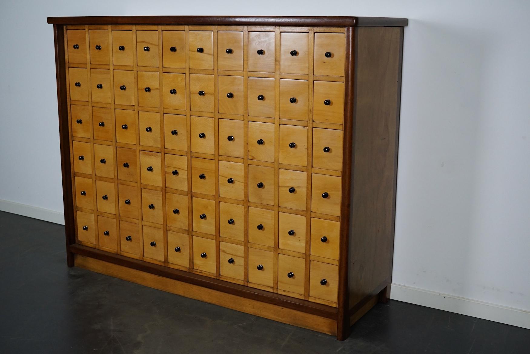 This apothecary cabinet was made circa 1950s in the Netherlands. The cabinet was used on a school to store painting supplies. It features 60 drawers with black metal knobs. The interior dimensions of the drawers are: D W H 37 x 9 x 13 cm.