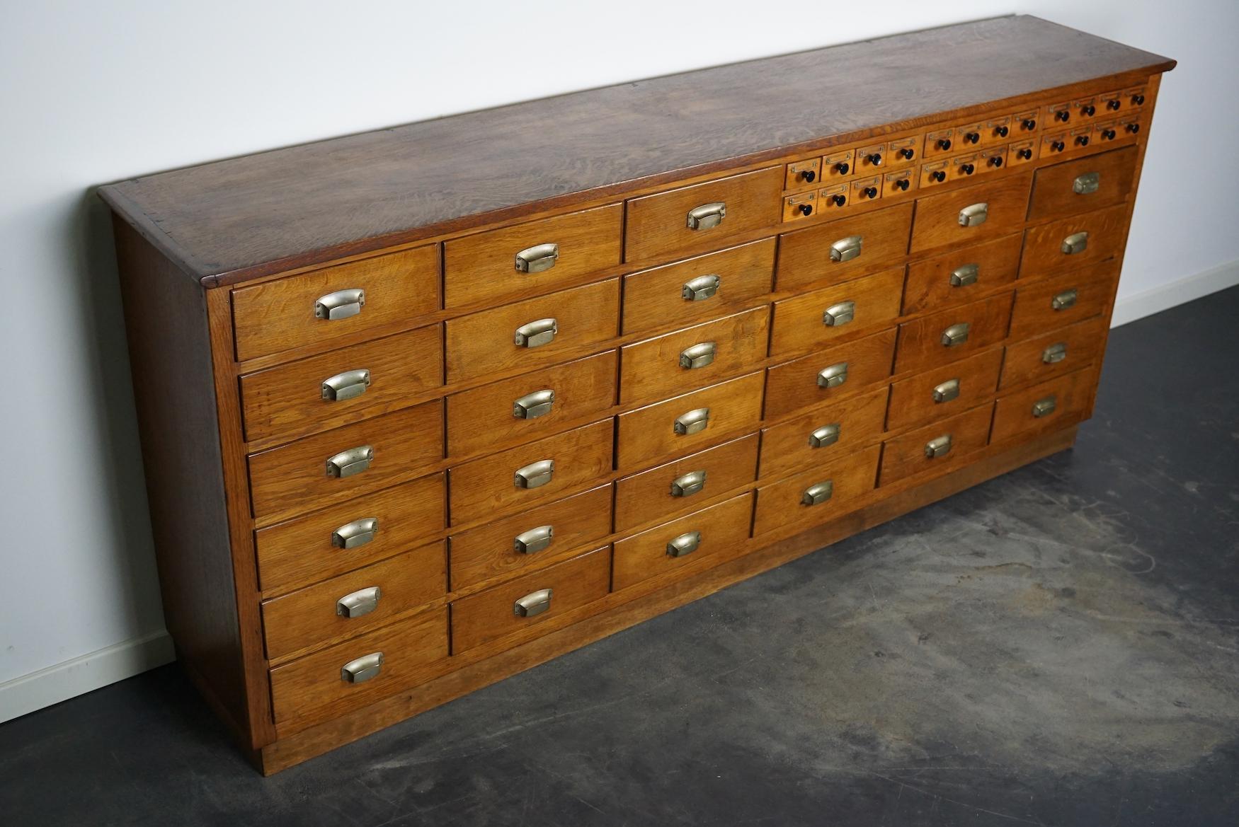 This apothecary cabinet was made circa 1940s in the Netherlands and used in a pharmacy until the 1990s. It features 33 large drawers with metal cup handles and 24 small ones with black knobs and metal name card holders.