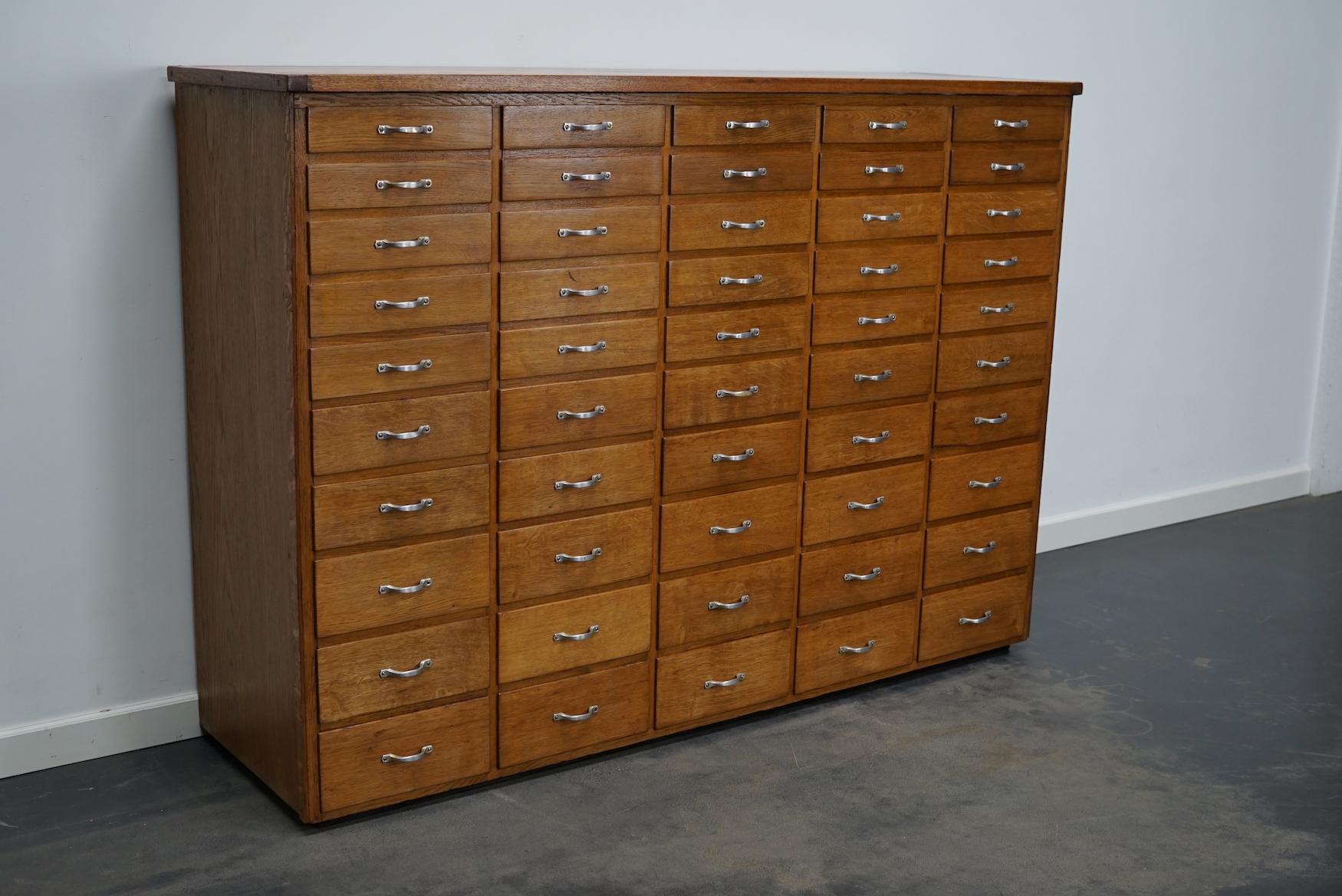 This apothecary cabinet was designed and made from oak circa 1950 in The Netherlands. It features 50 drawers in four different sizes with metal hardware. The inside of the drawers measure: DWH 36 x 23 x 3 / 4.5 / 6 / 8 cm.